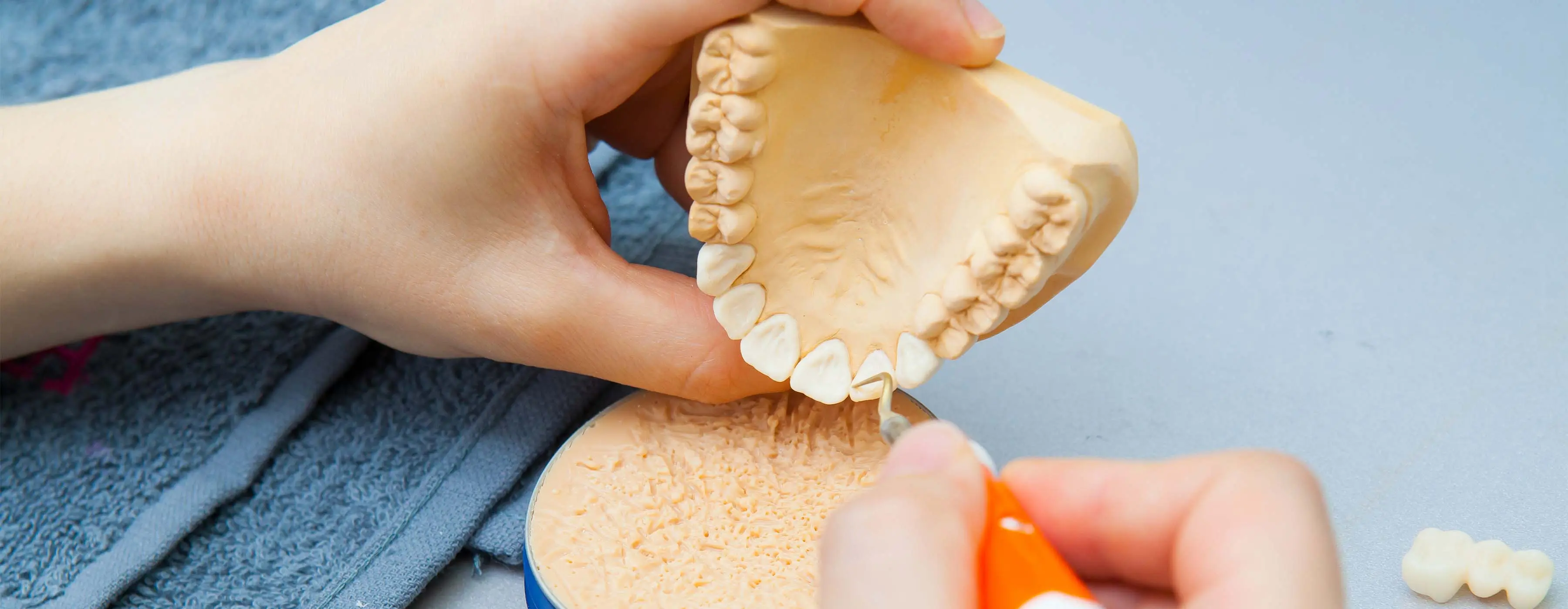 Foto em close de mãos com luvas cirúrgicas manipulando uma prótese dentária utilizando ferramentas de odontologia.