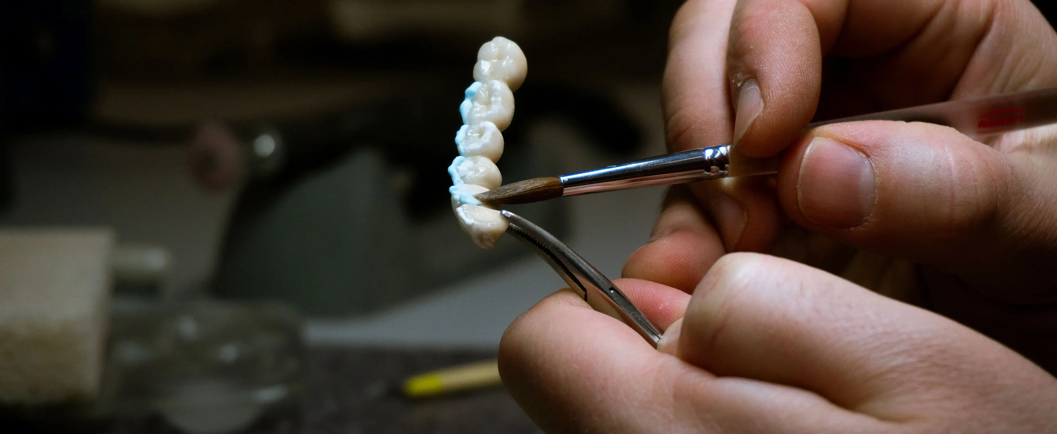 Foto em close de mãos manipulando uma prótese dentária utilizando ferramentas de odontologia.