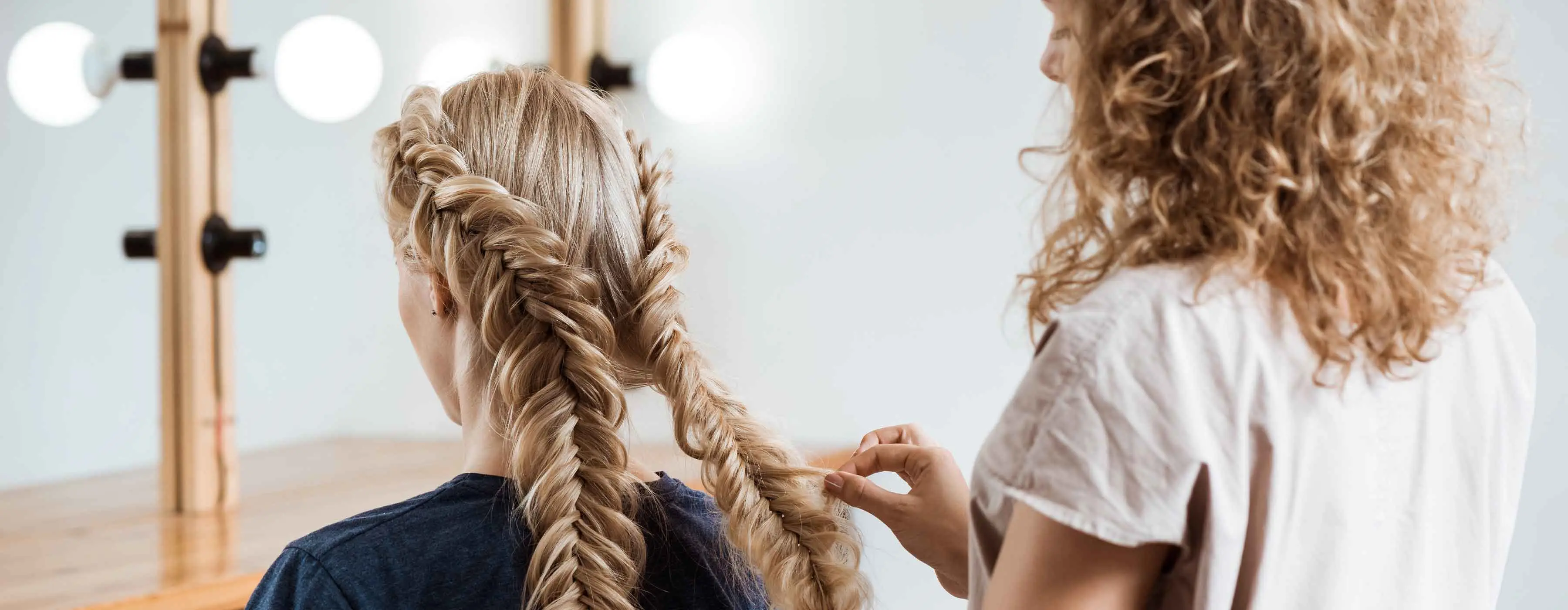Foto de uma mulher trançando o cabelo loiro de outra.