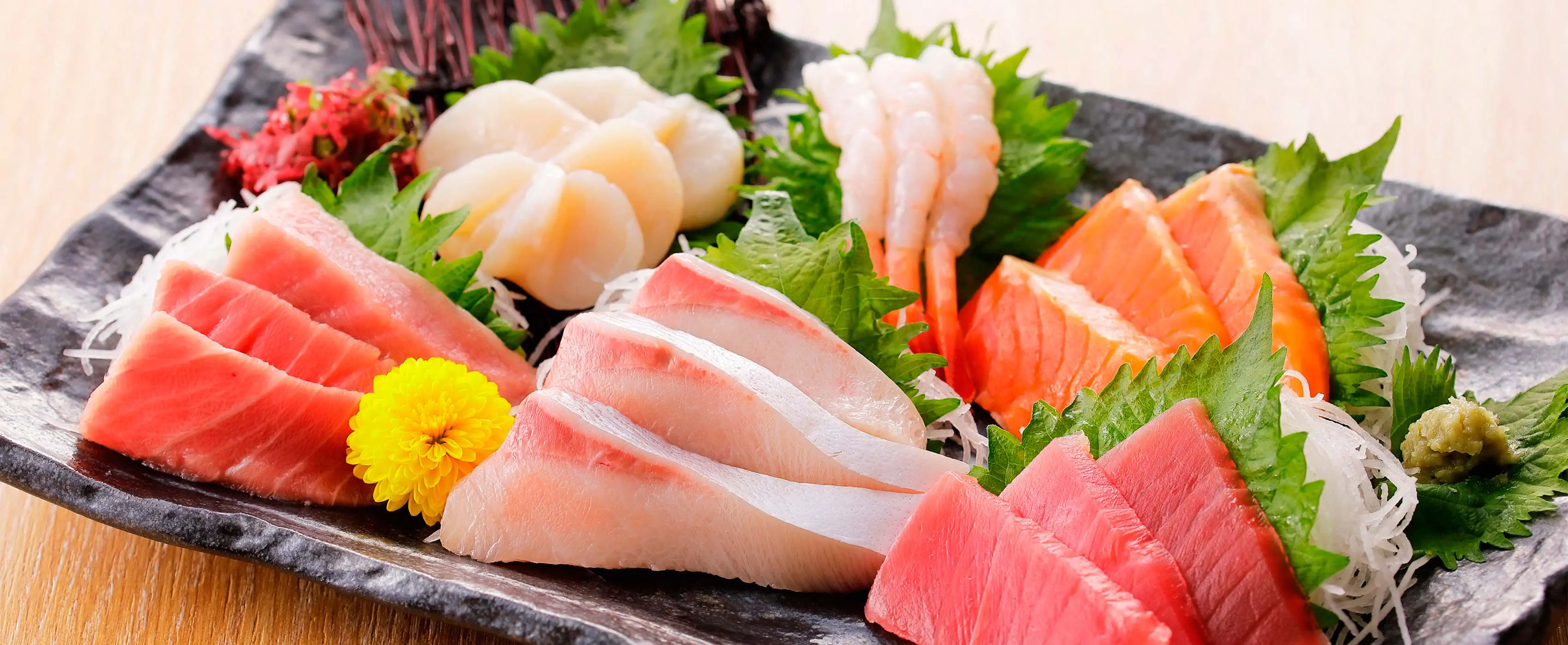 Foto em close de prato de sushis e sachimis enfeitado com folhas e flores.