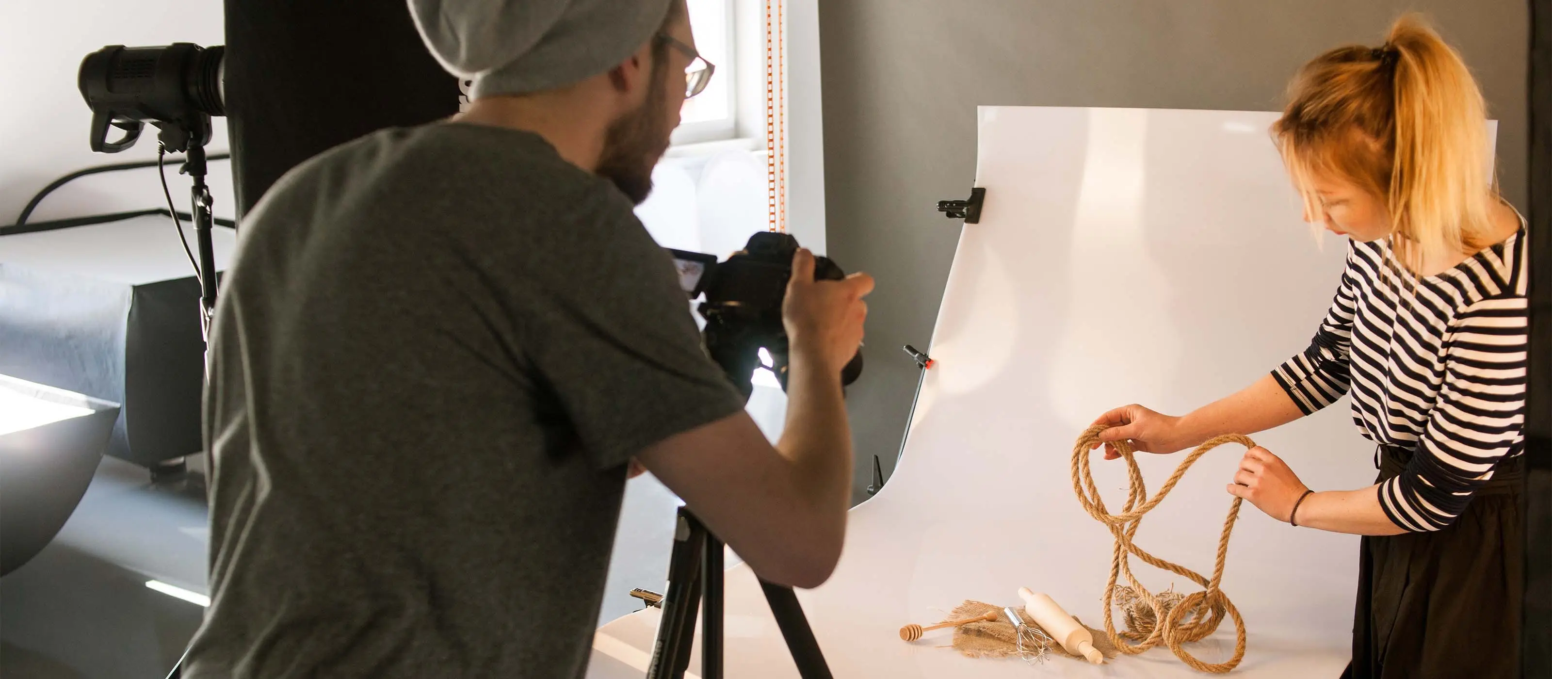 Foto de um homem manuseando uma câmera fotográfica enquanto uma mulher na frente arruma os objetos do cenário para a foto.
