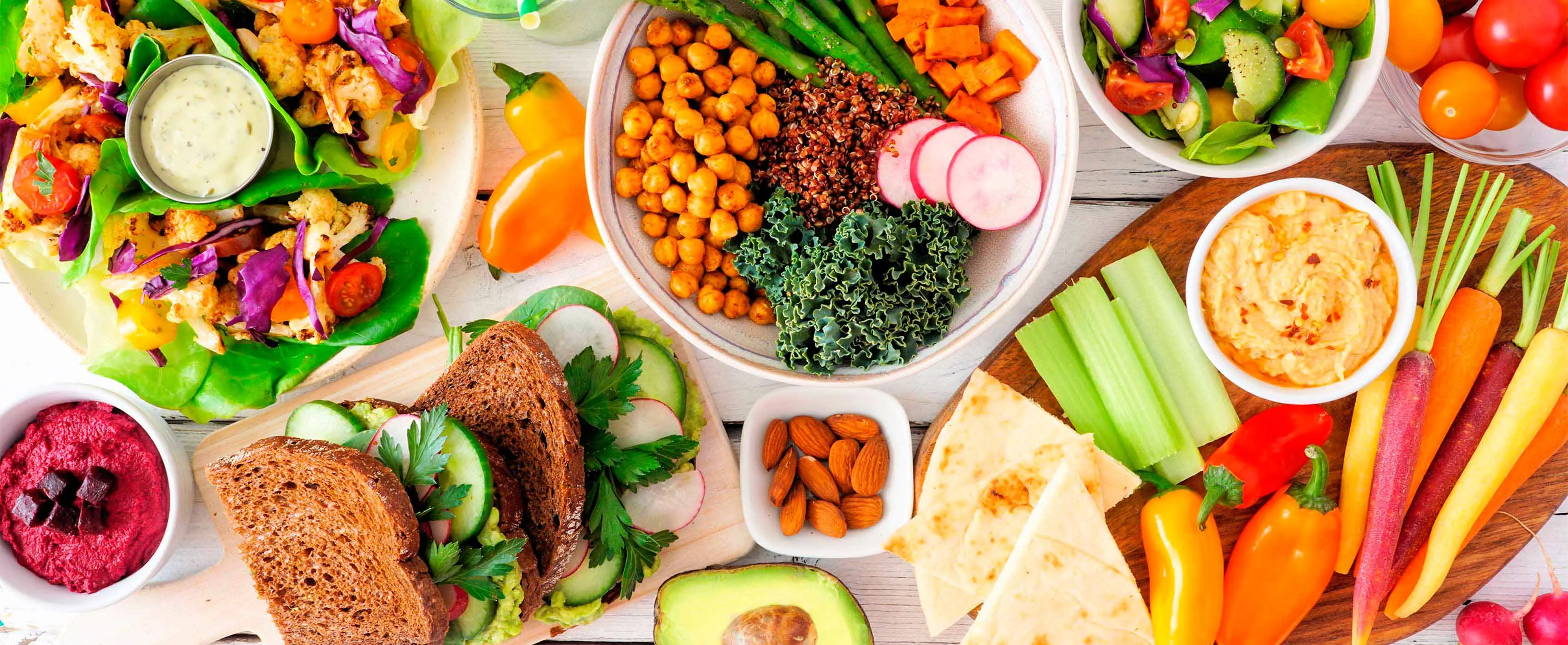 Foto de pratos com saladas e sanduíches naturais junto com frutas em mesa.