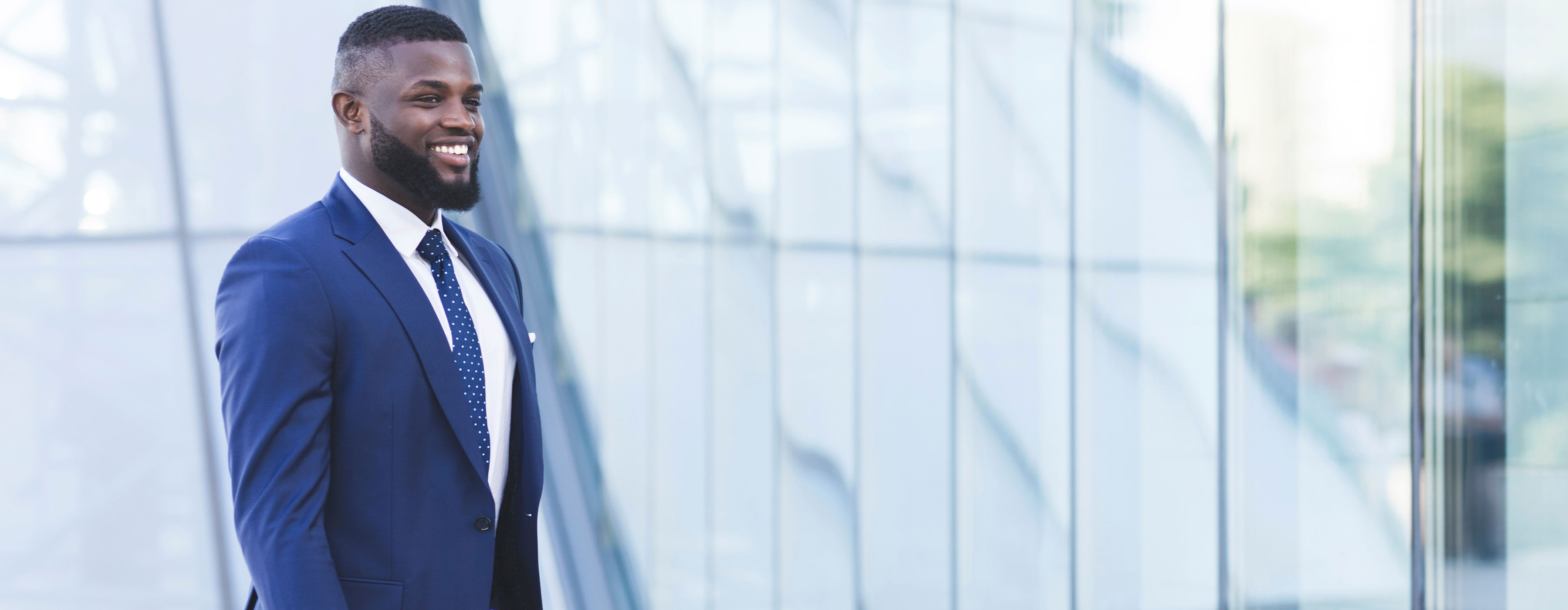 Empreendedorismo Digital - foto de um homem vestindo terno azul com gravata de bolinhas brancas,  em pé diante de uma fachada de vidro, refletindo a luz natural.