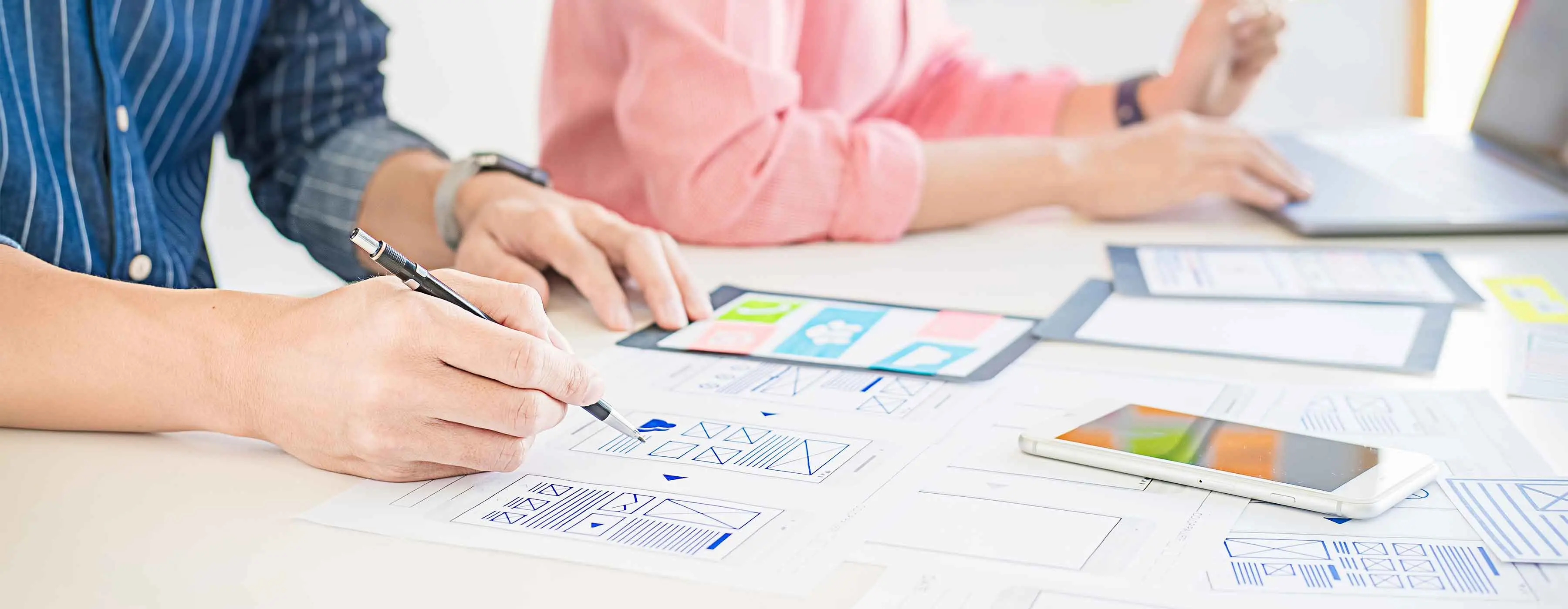 Em uma mesa, há desenhos de wireframes feitos à mão.