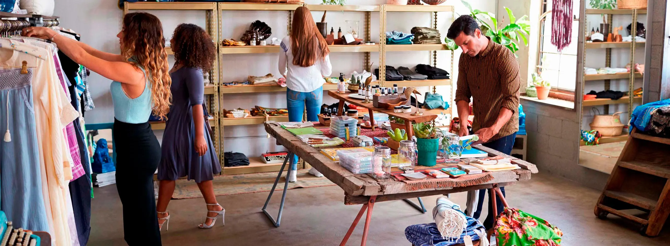 Foto de grupo de pessoas em ambiente com bancada de produtos, prateleiras e arara de roupas.