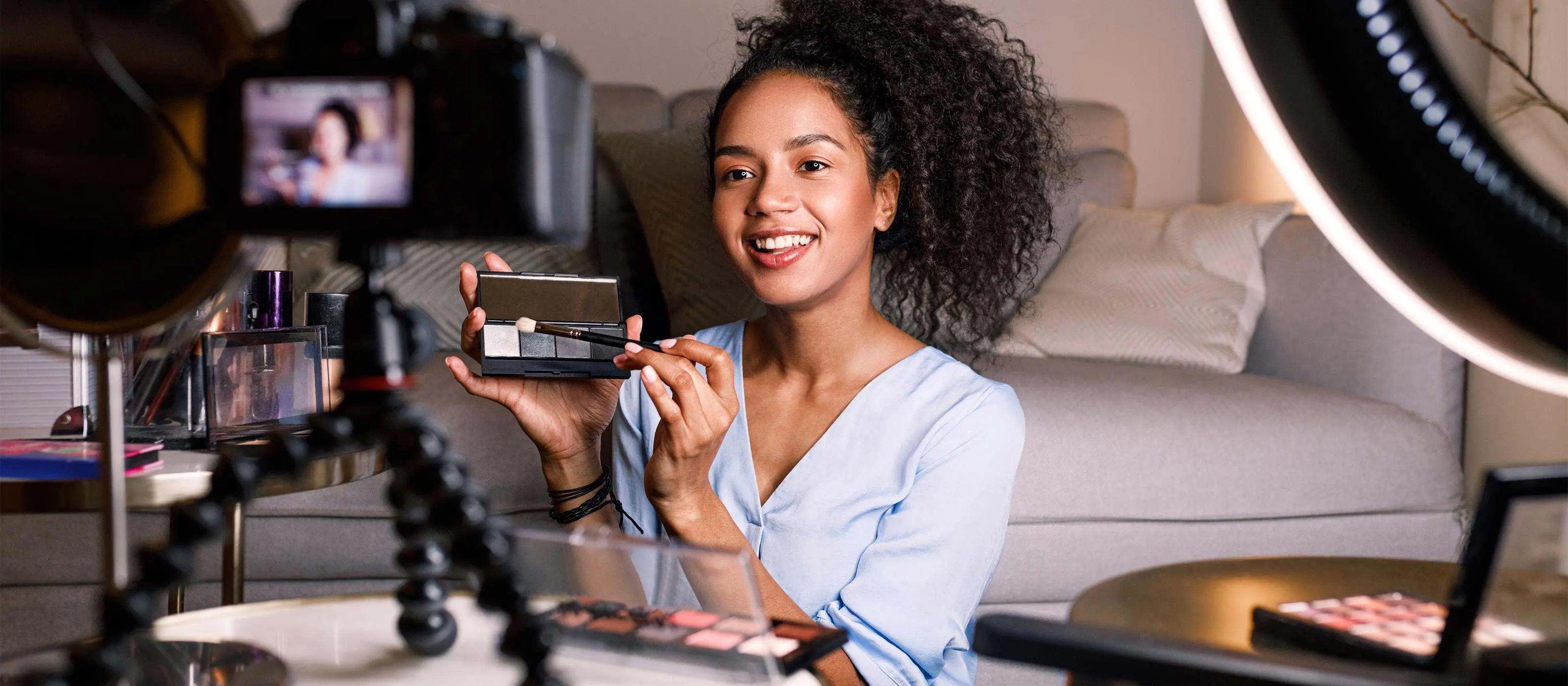 Foto de uma moça gravando vídeo tutorial para uso de maquiagem.