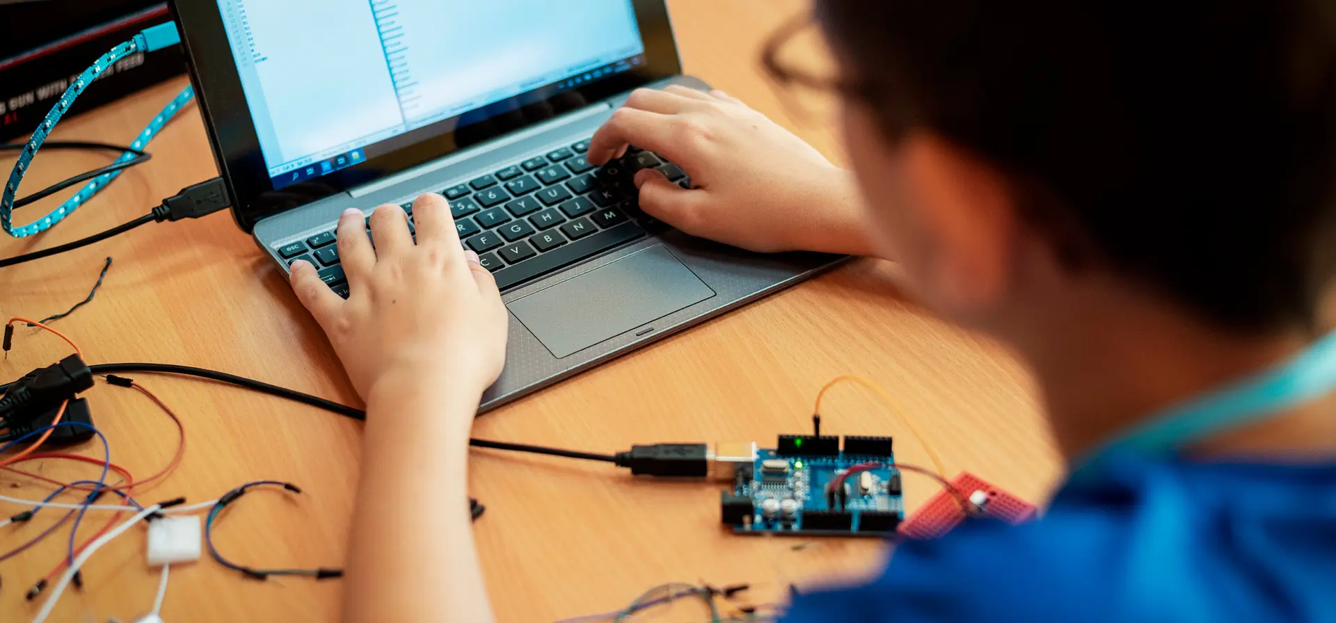 Foto de homem de costas, mexendo em um notebook com peças e fios expostos.