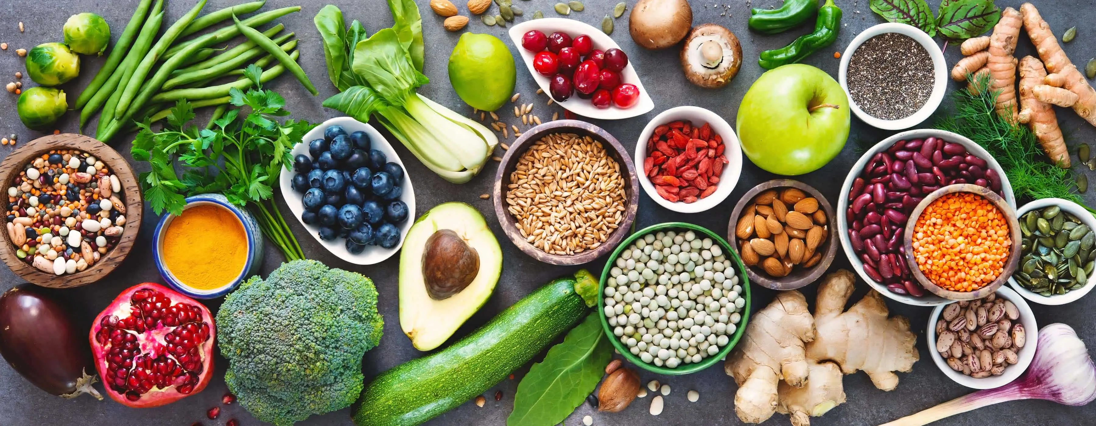 Fotos de frutas, verduras e legumes em mesa junto com potes com cereais, temperos e castanhas e grãos.