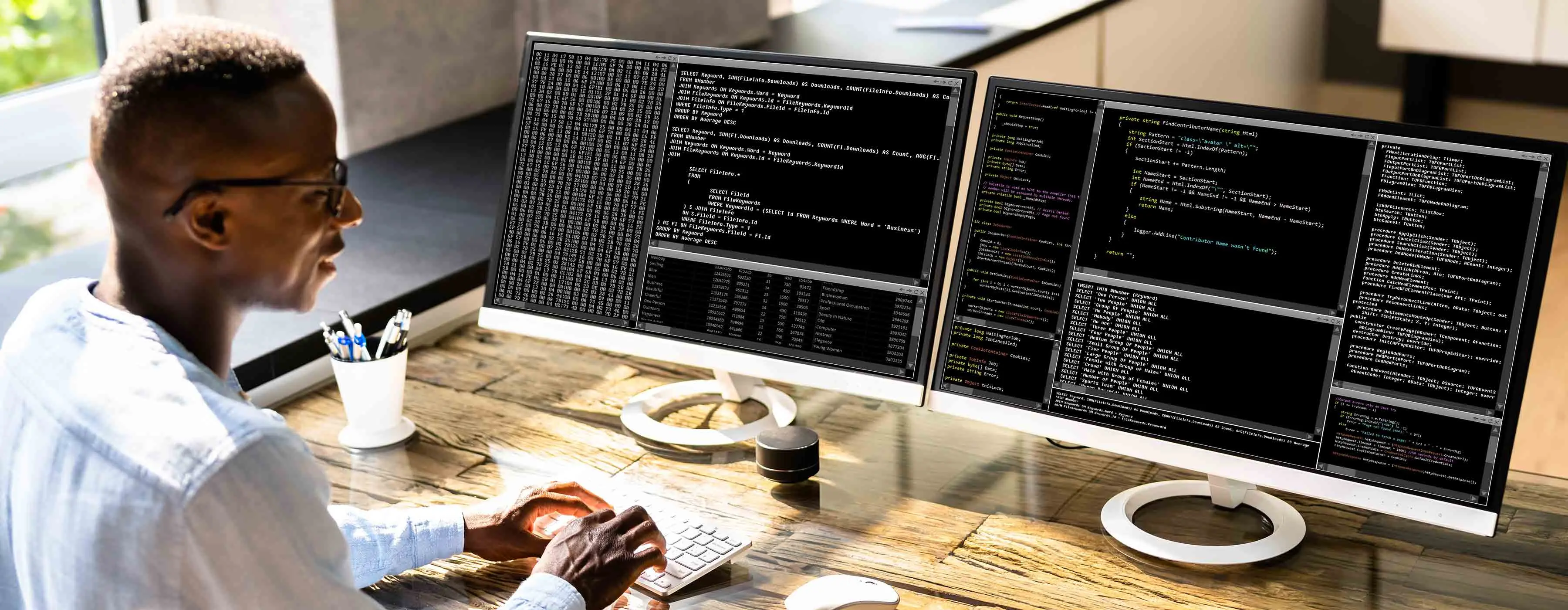 Foto de homem com dois monitores de computador que exibem códigos de programação.