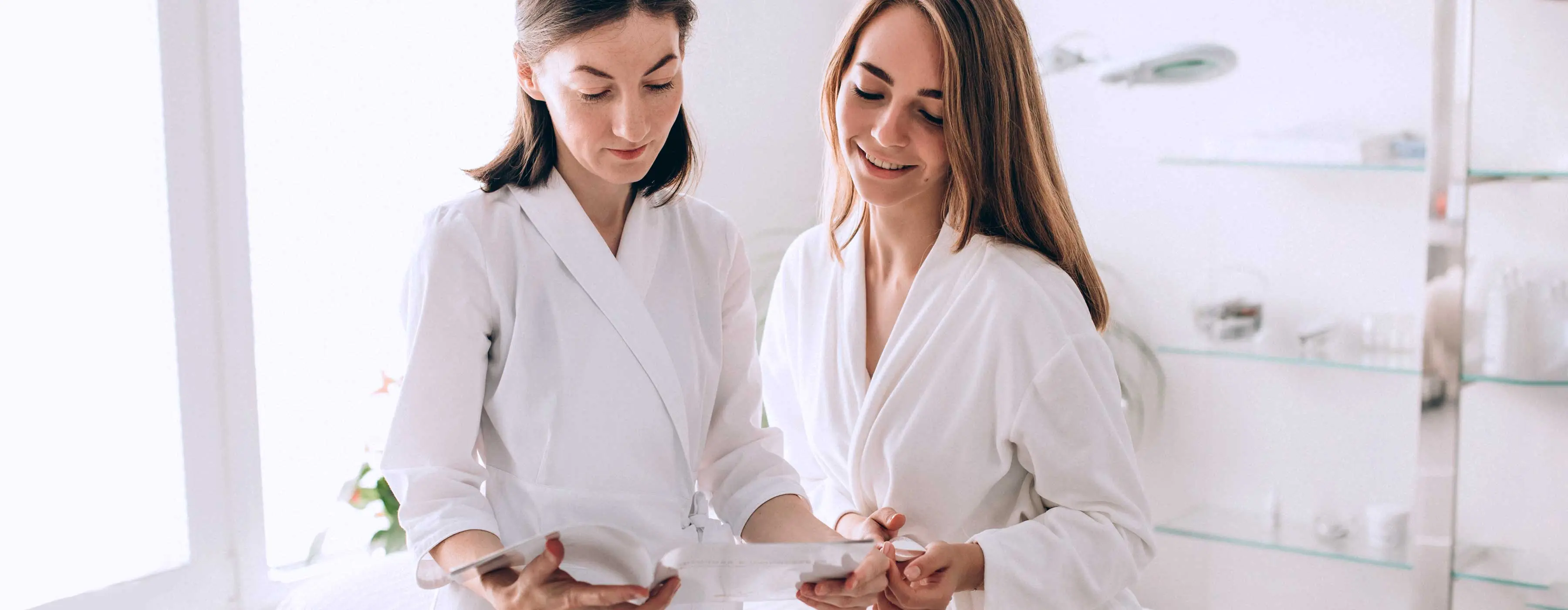 Avaliação da Saúde do Cliente na Área de Estética - Foto de duas mulheres de branco lendo um documento em salão de estética.