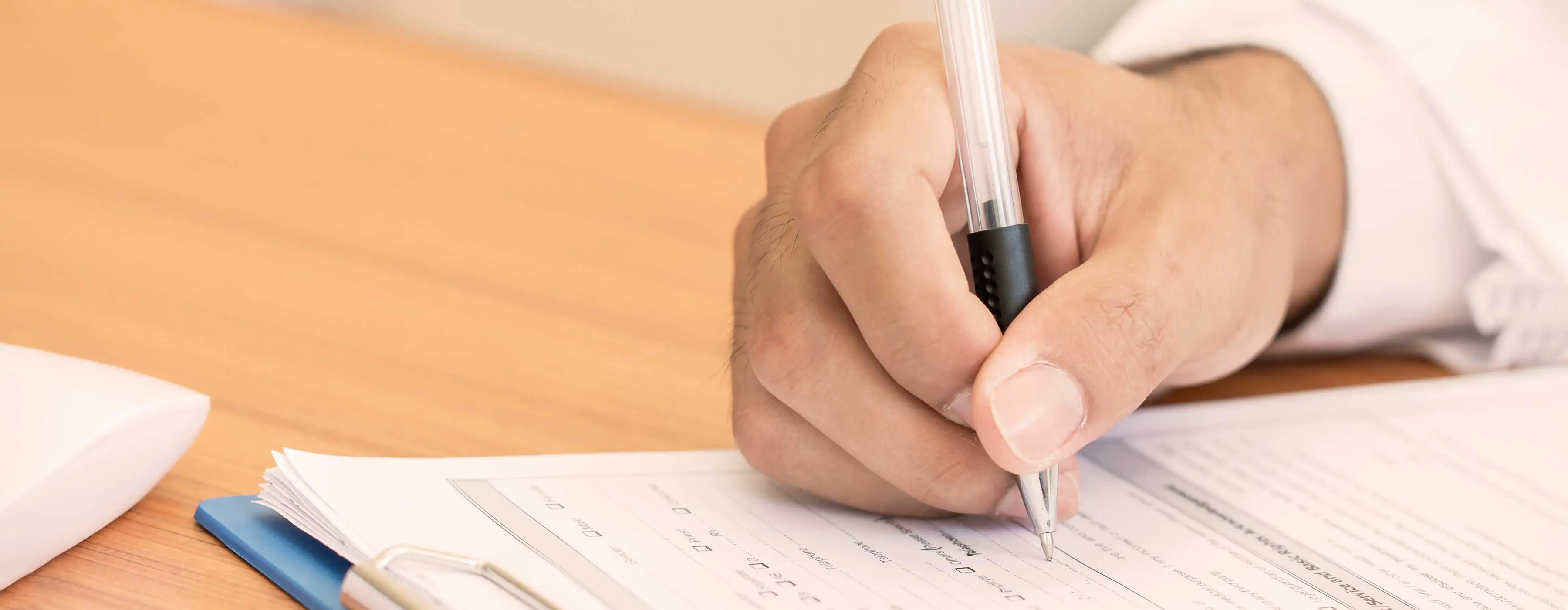Foto de mão de uma pessoa assinando formulário de atendimento em mesa de escritório.