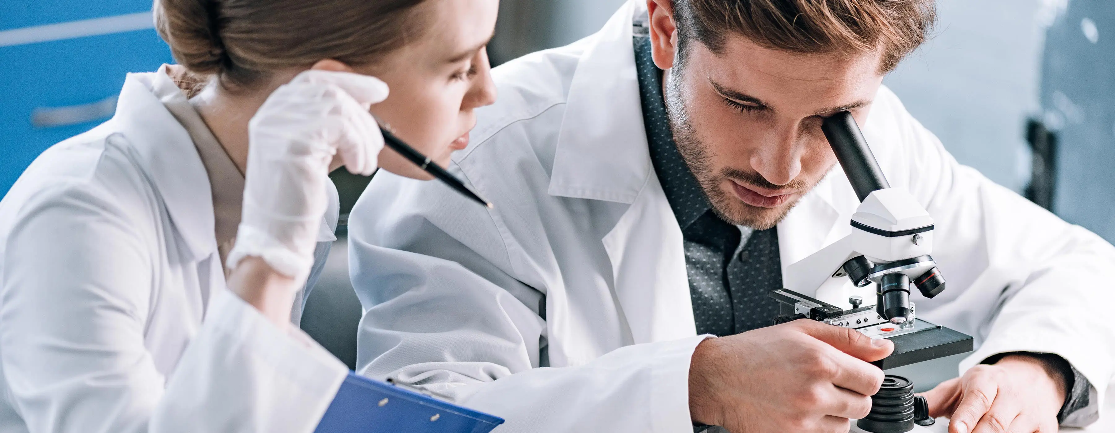 Foto de duas pessoas observando em microscópio substância em laboratório.