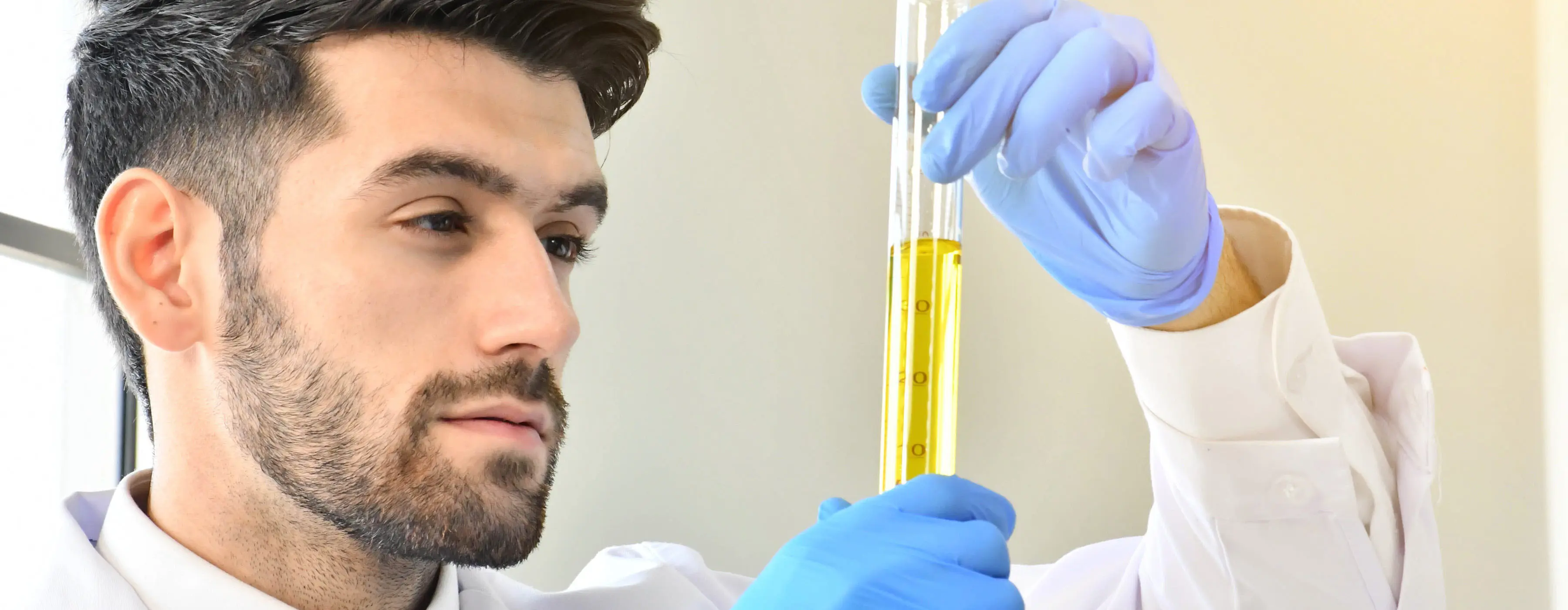 Foto de homem observando tubo de ensaio teste de óleo lubrificante em indústria química.