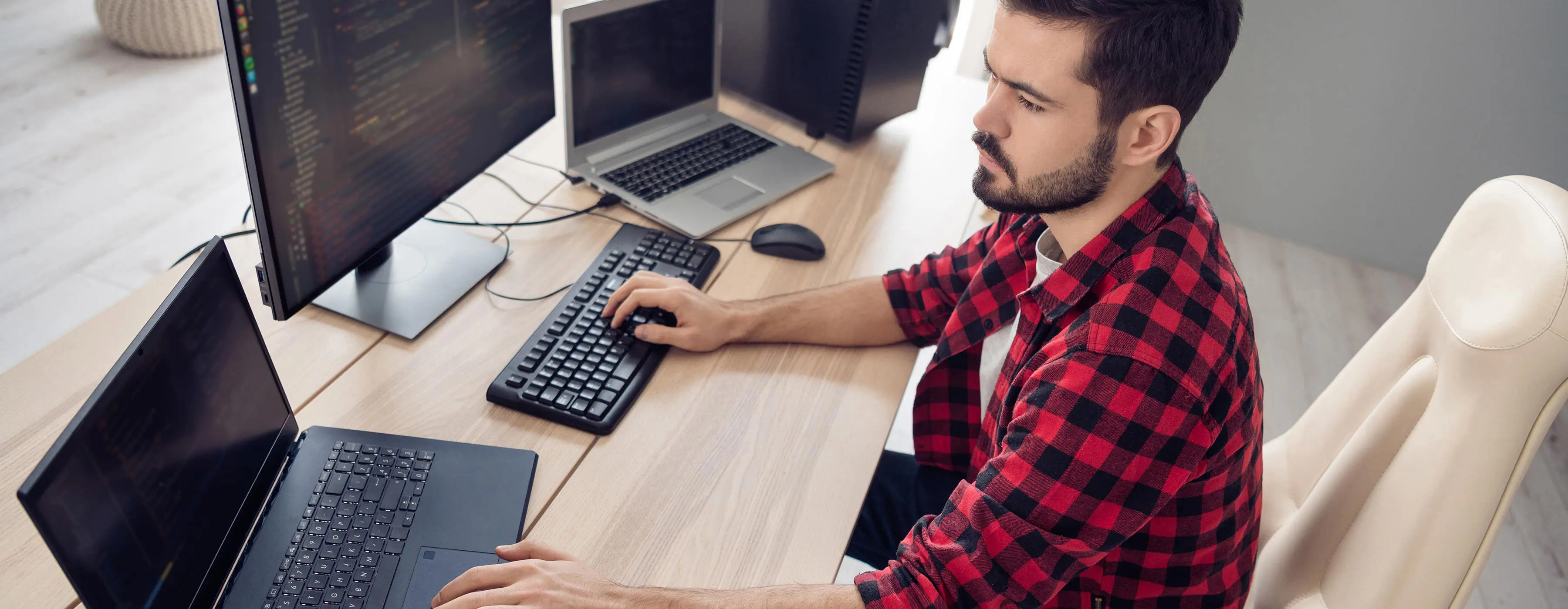 Foto de jovem programando em notebook e computador em escritório.