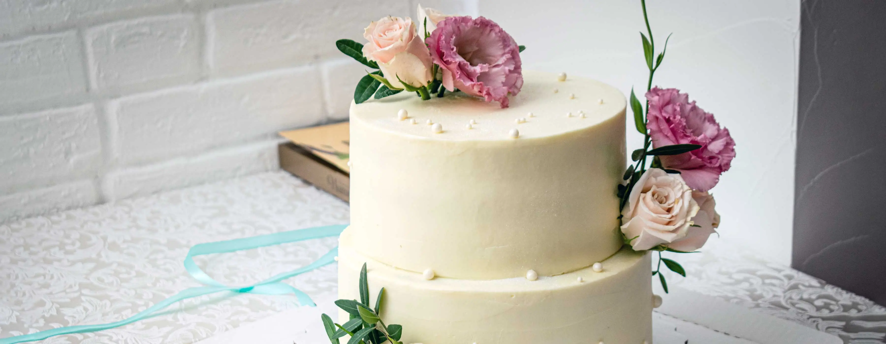 Foto de um bolo branco de casamento de dois andares enfeitado com flores de açúcar comestíveis em cima de uma mesa.