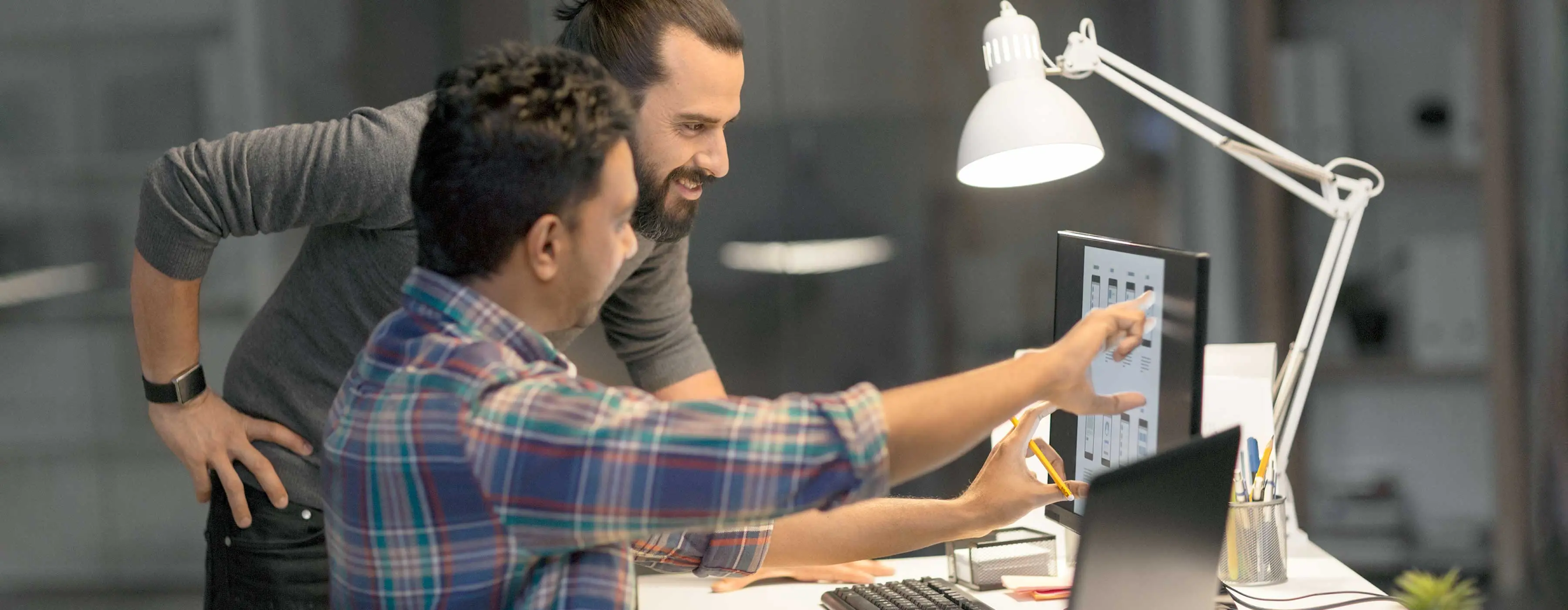 Foto de dois homens sorrindo e olhando para tela de computador.