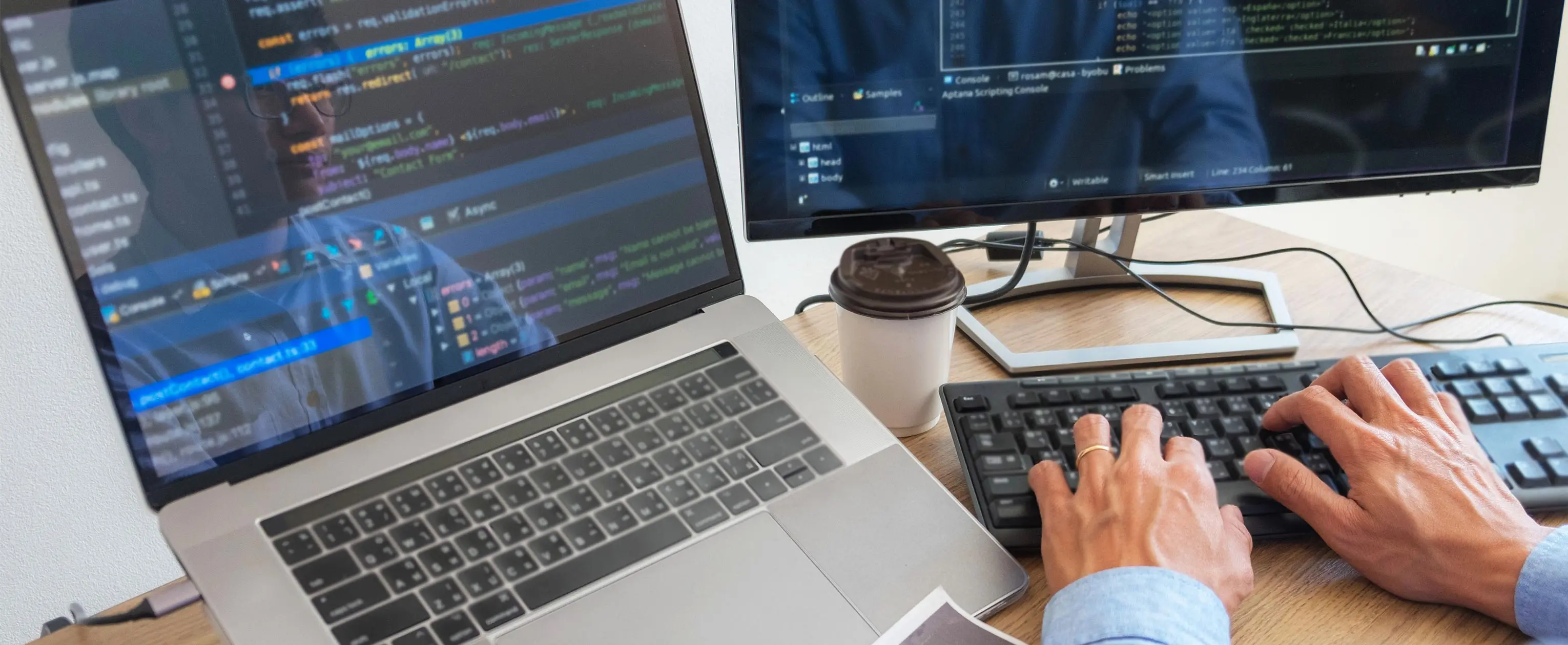 Foto enfoca mãos de uma pessoa digitando códigos em computador, ao lado de notebook com códigos de programação.