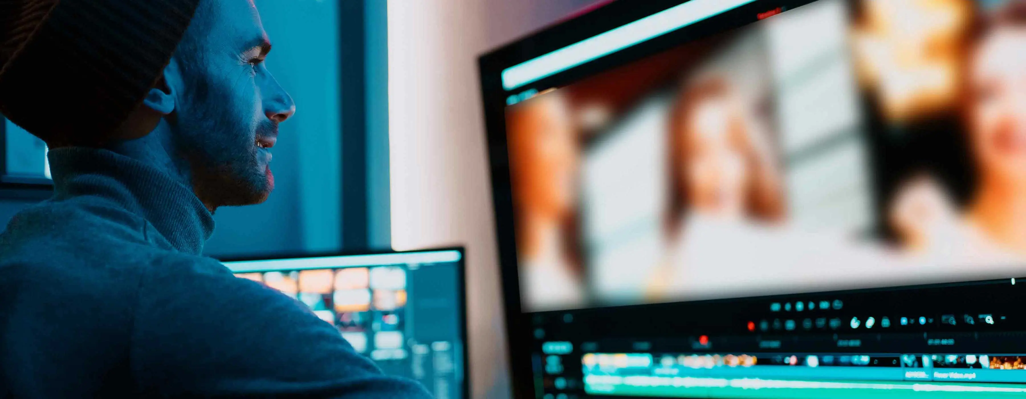 Foto de homem olhando sorridente para tela de computador que exibe software de edição de vídeo.