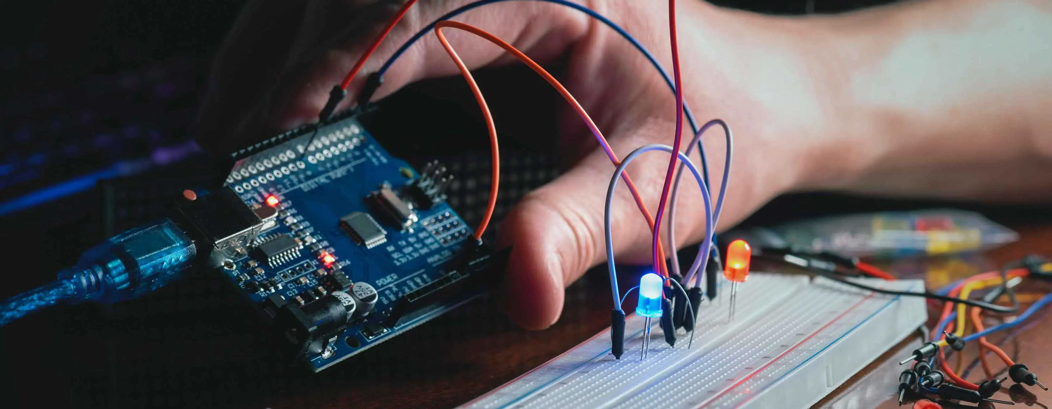 Foto de mão segurando componente eletrônico com fios e luzes coloridas.