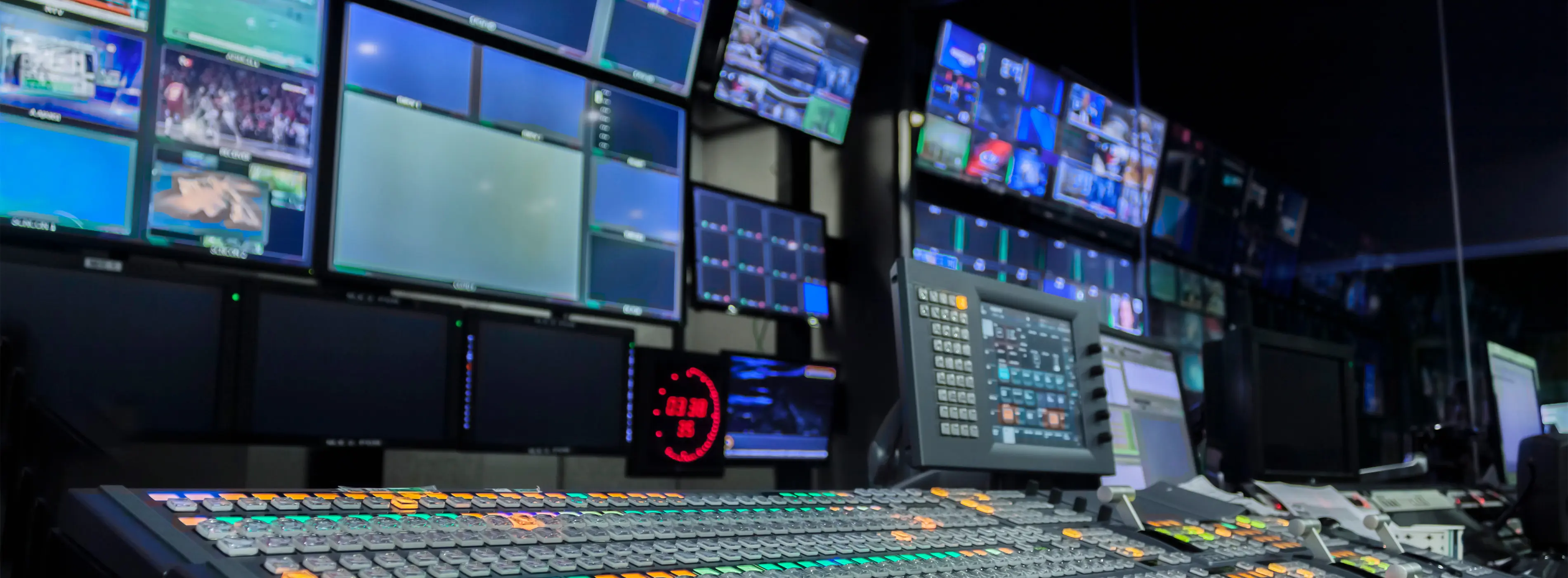Foto de estúdio de TV com equipamentos e monitores utilizados para direção de áudio e vídeo.