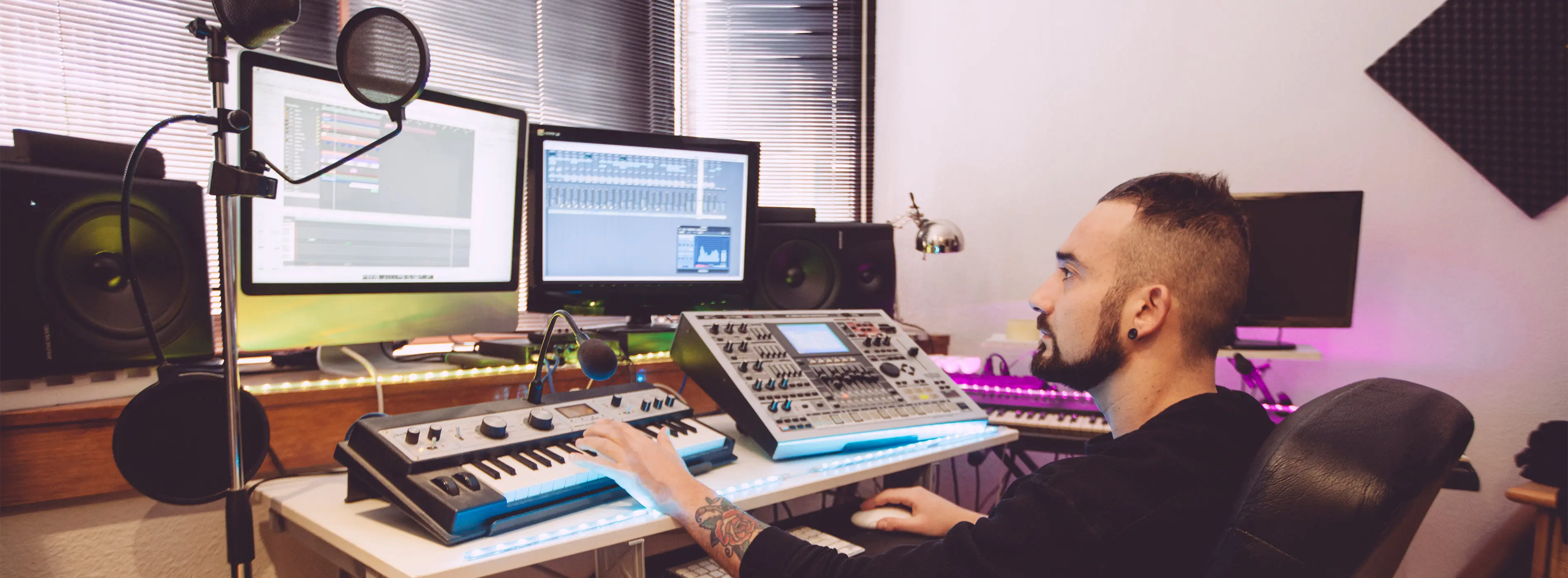 Foto de homem tocando teclado e observando tela de computador em estúdio musical.