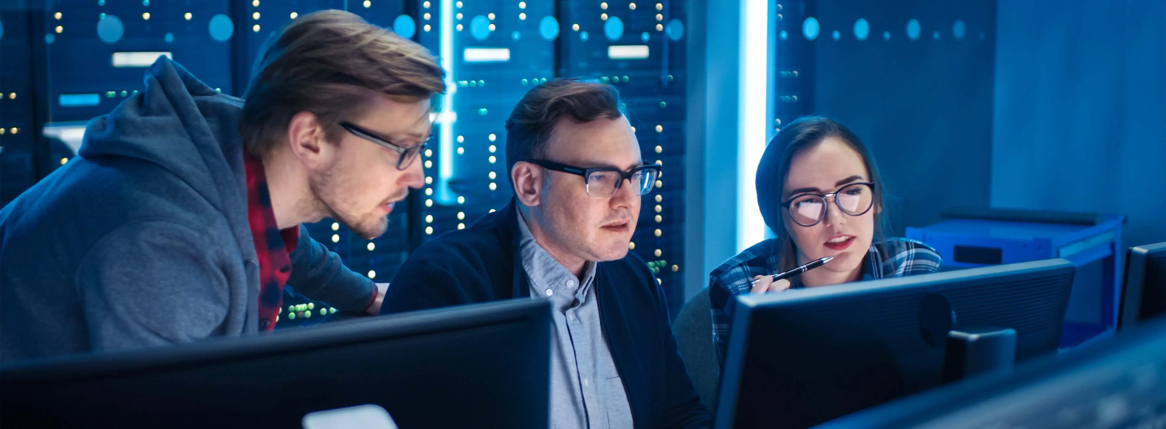 Foto de três pessoas conversando em frente a computadores e telas em um data center.