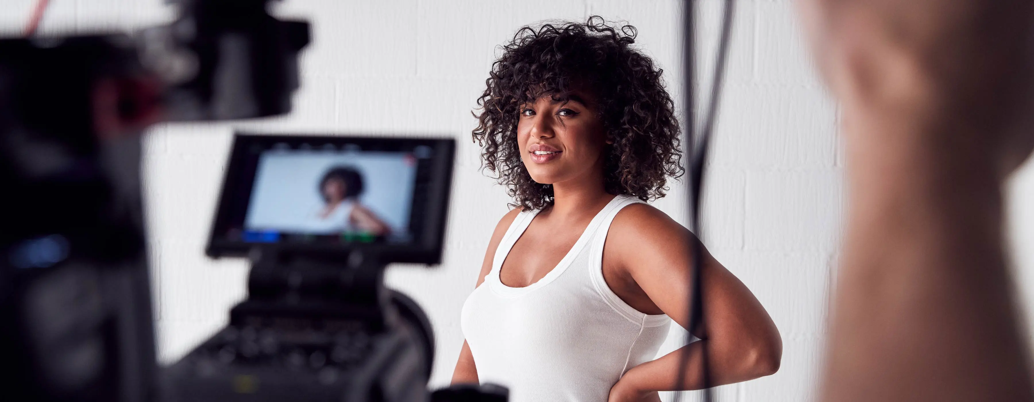 Foto em plano fechado de uma modelo sendo fotografada. Em primeiro plano, display de máquina fotográfica reflete pose que modelo está fazendo.