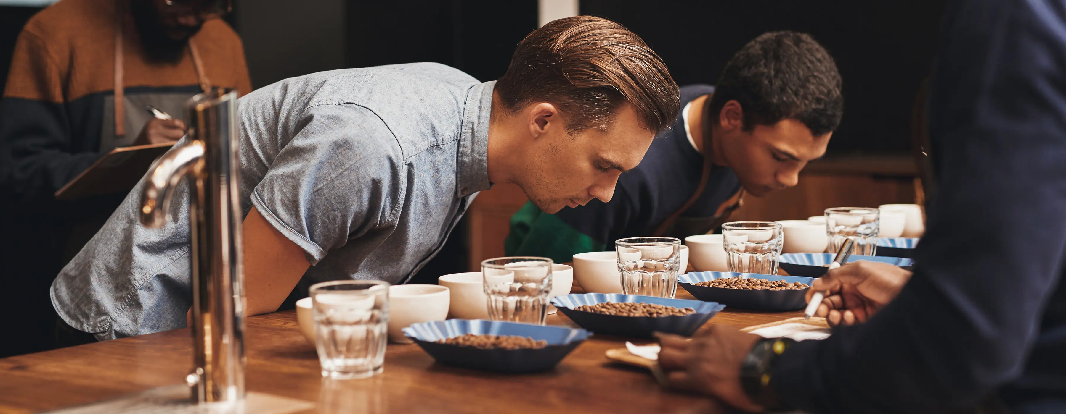 Foto de dois homens fazem avaliação sensorial de grãos de café dispostos em uma mesa