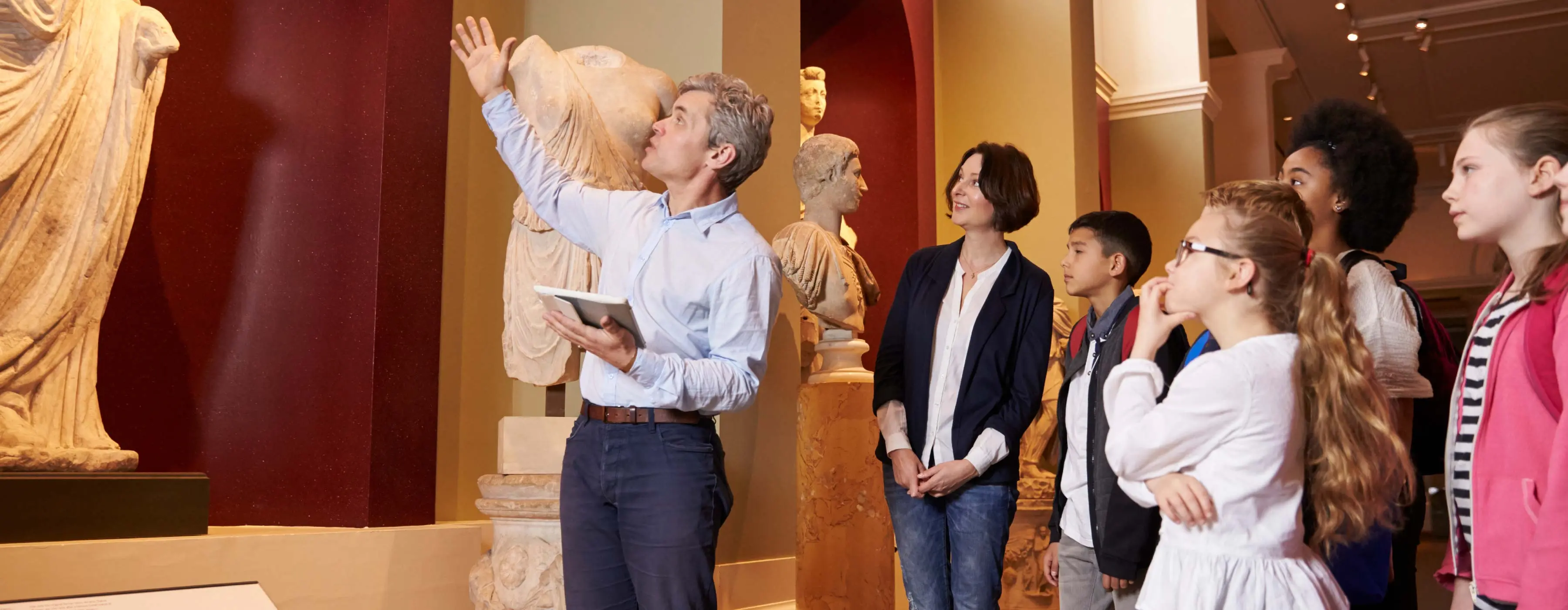 Foto de um profissional de turismo apresentando uma estátua para grupo de pessoas em um cenário de museu.