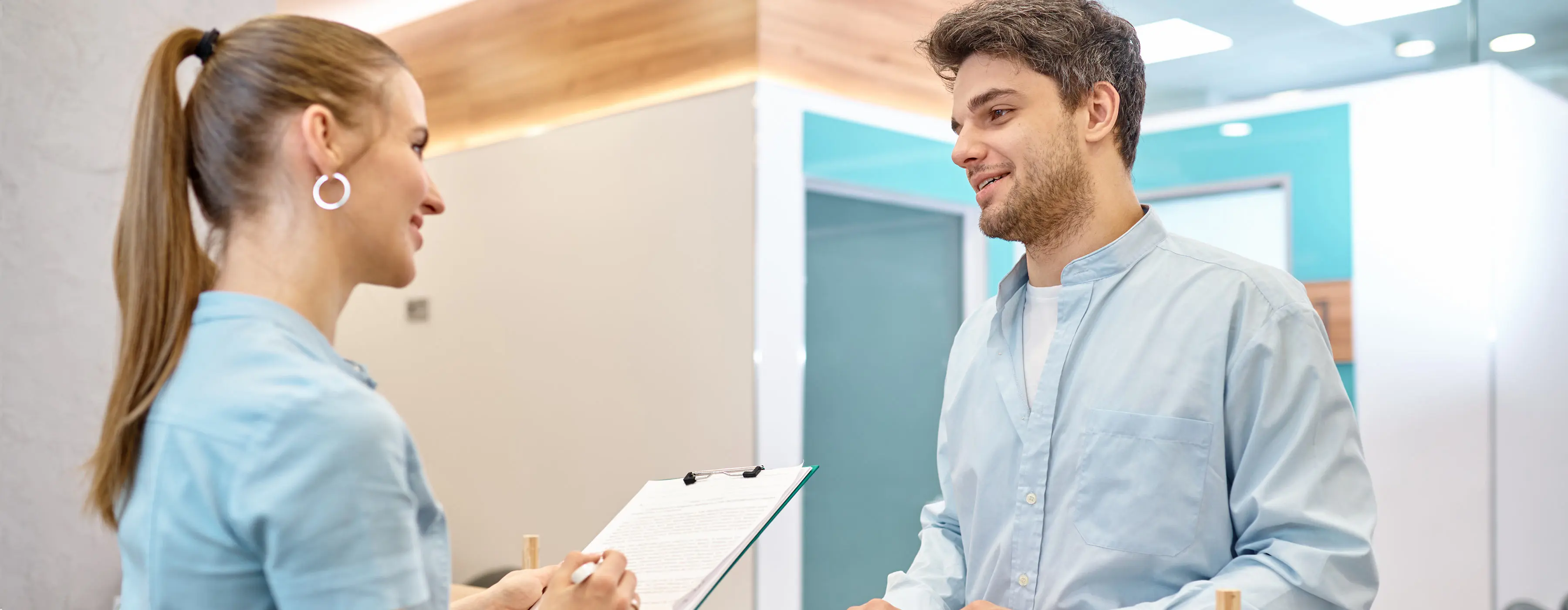 Foto de uma mulher conversando com homem e fazendo anotações em uma prancheta.