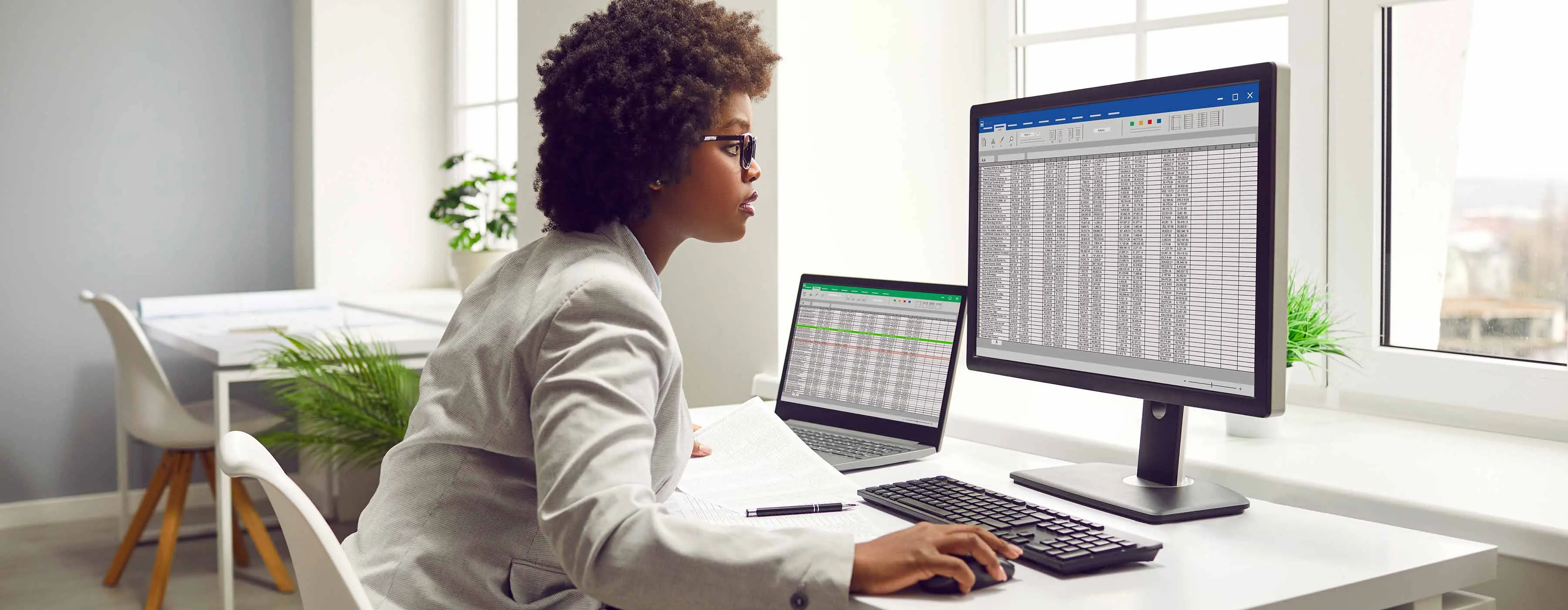 Foto de mulher usando óculos olha para tela de computador que exibe uma tabela Excel