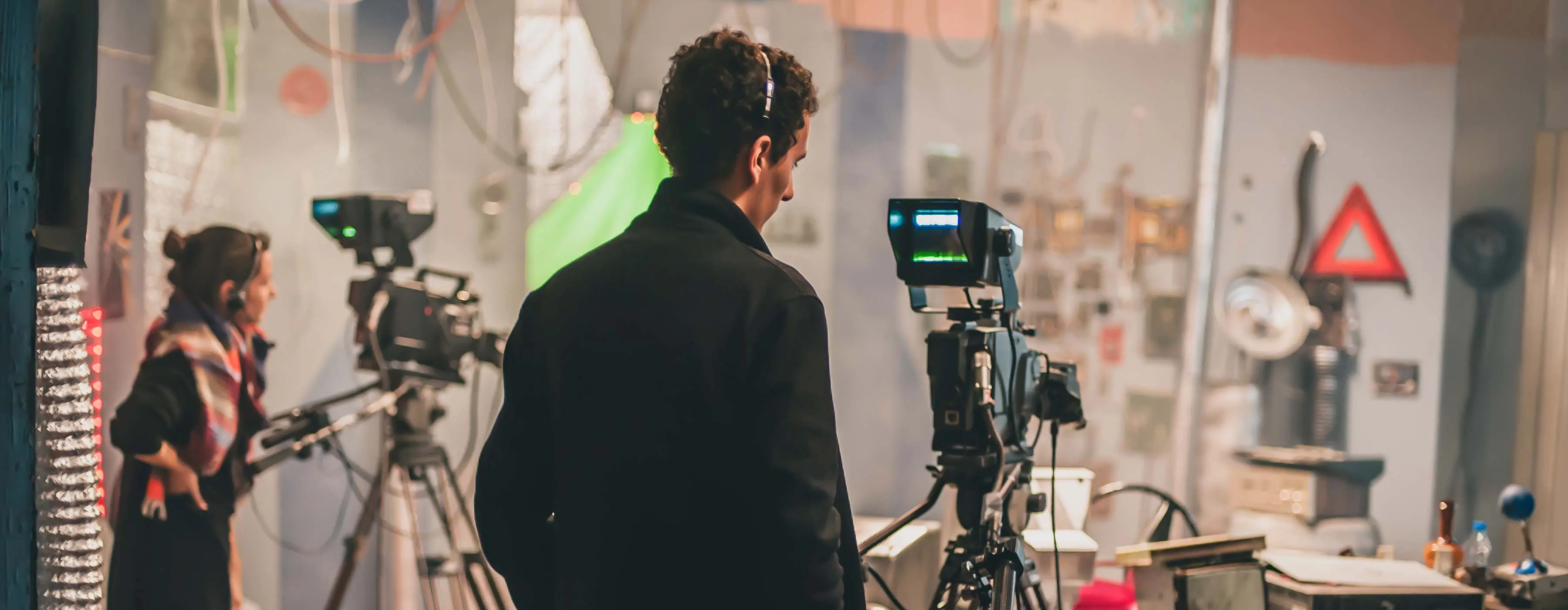 Foto de homem de casaco preto, com fone de ouvido observando uma câmera em set de filme