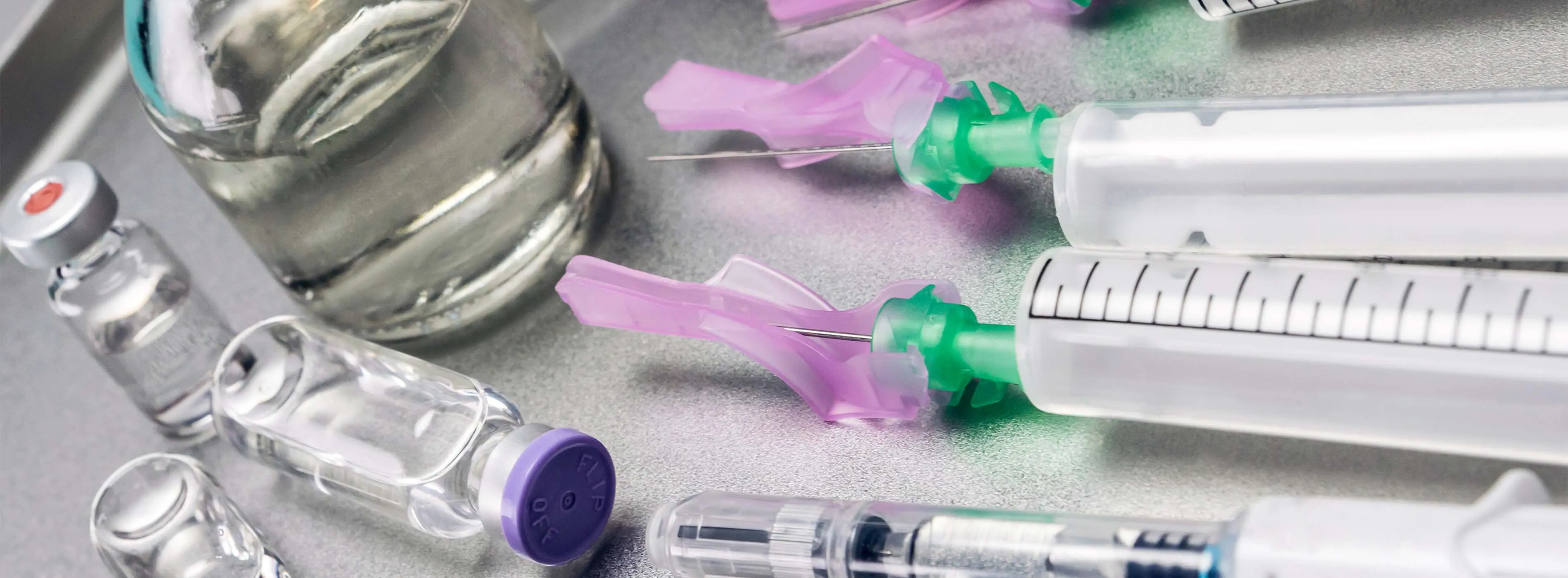 Foto em close de seringas e tubos pequenos de medicação em uma mesa metalizada