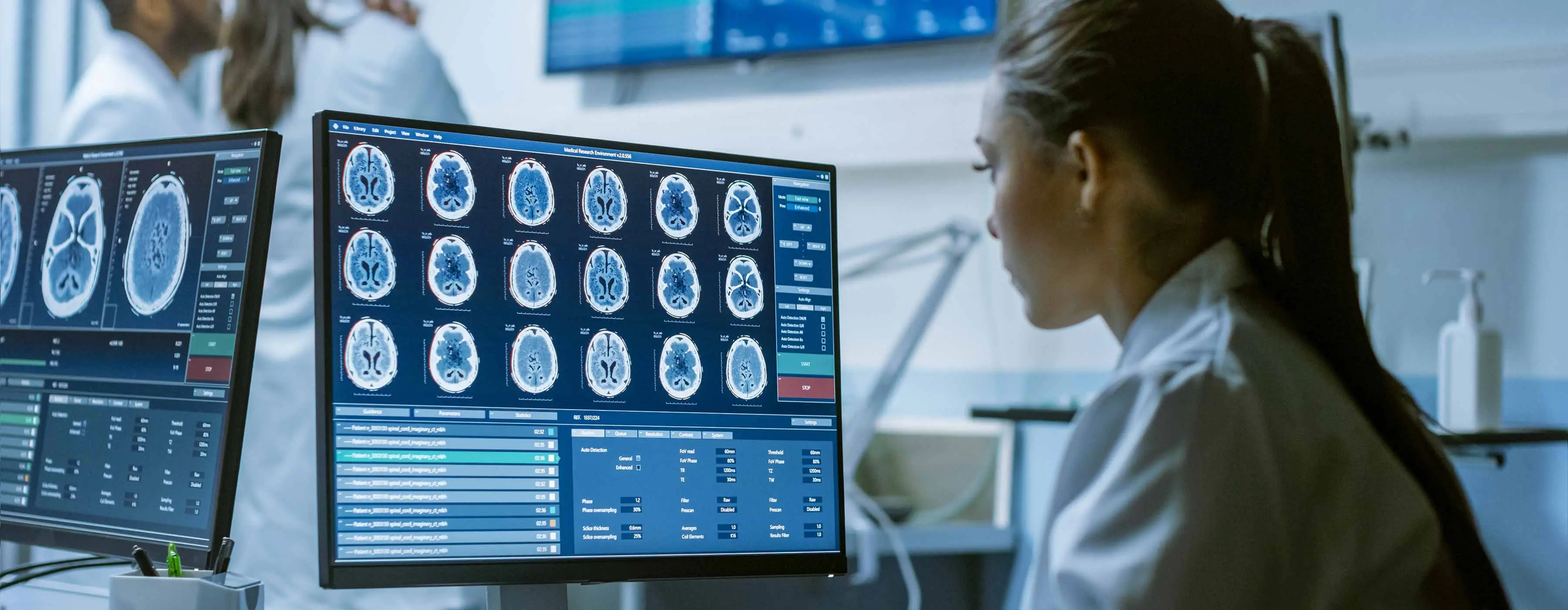 Foto em close de profissional da saúde olhando para telas de computadores com imagens de exames, em ambiente hospitalar