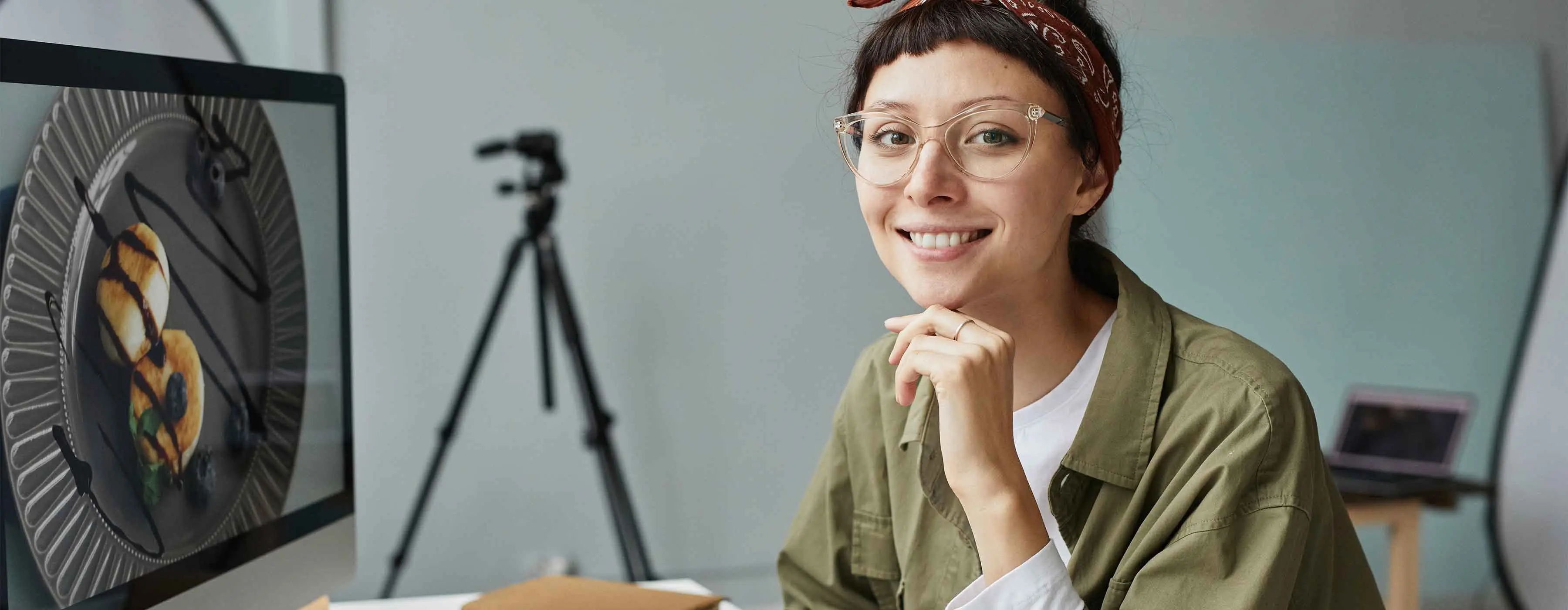 Foto de uma mulher sorrindo enquanto edita uma foto de sobremesa no computador.