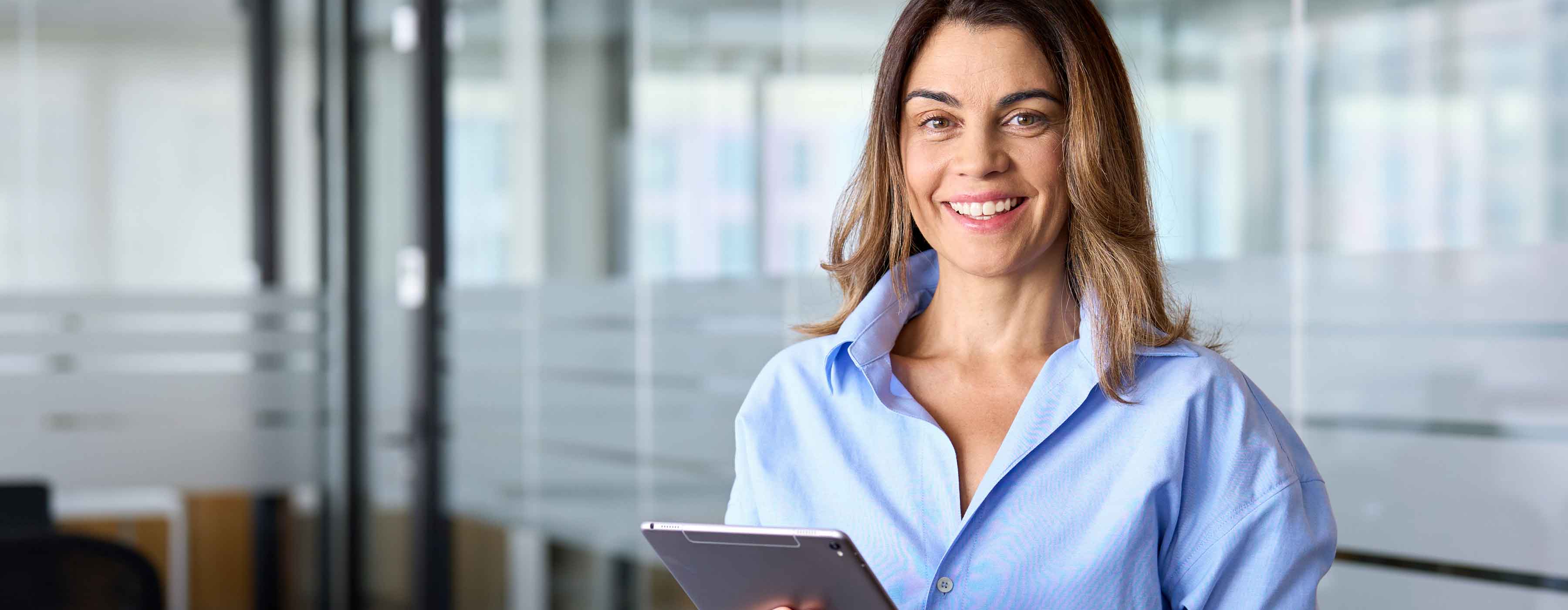 Gestão Condominial: operação e manutenção - foto de uma mulher sorridente segurando um tablet em um ambiente com paredes de vidro.