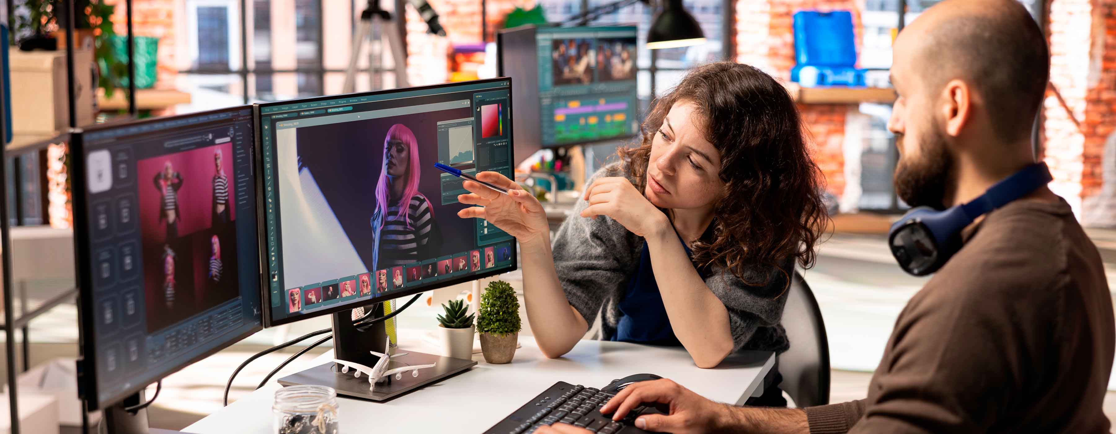 Publicidade inteligente: inteligência artificial aplicada ao conteúdo - foto de um homem usando o computador com duas telas e uma mulher conversando com ele e apontando para a imagem na tela do computador.
