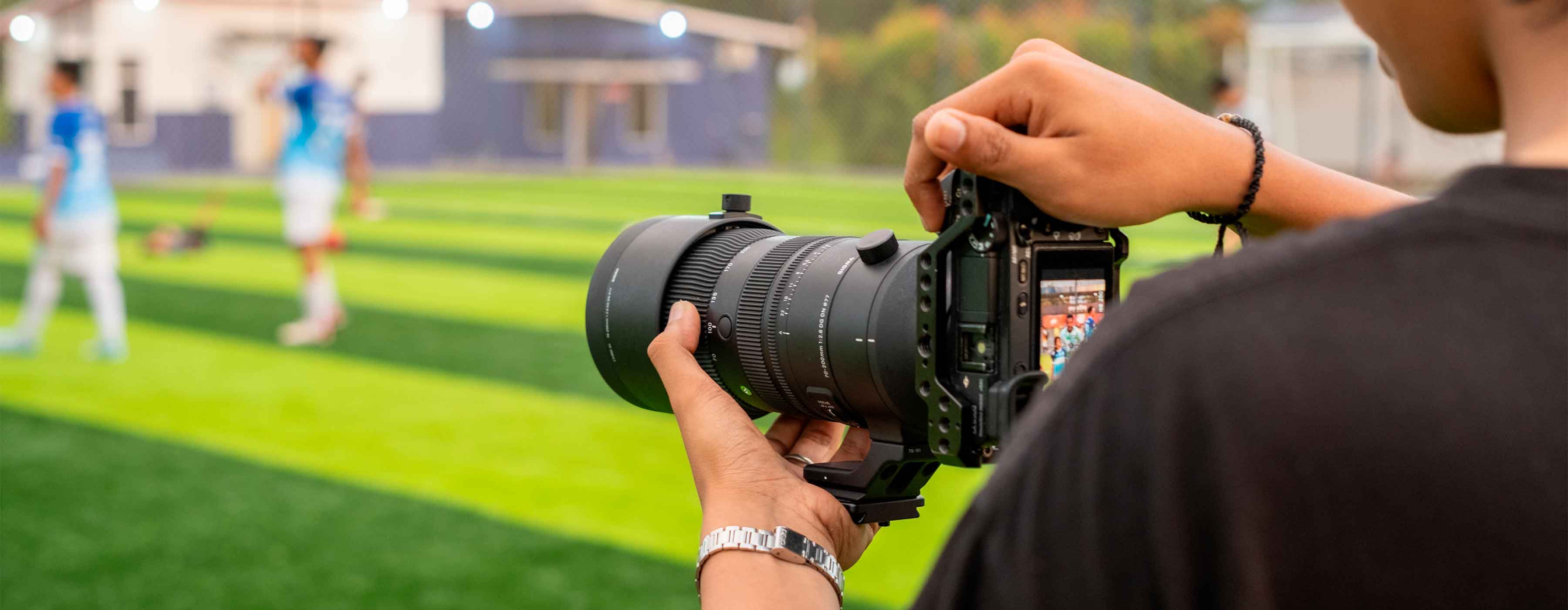 Introdução à Fotografia Esportiva - foto de uma pessoa com câmera fotográfica à beira de um campo gramado fotografando atletas.