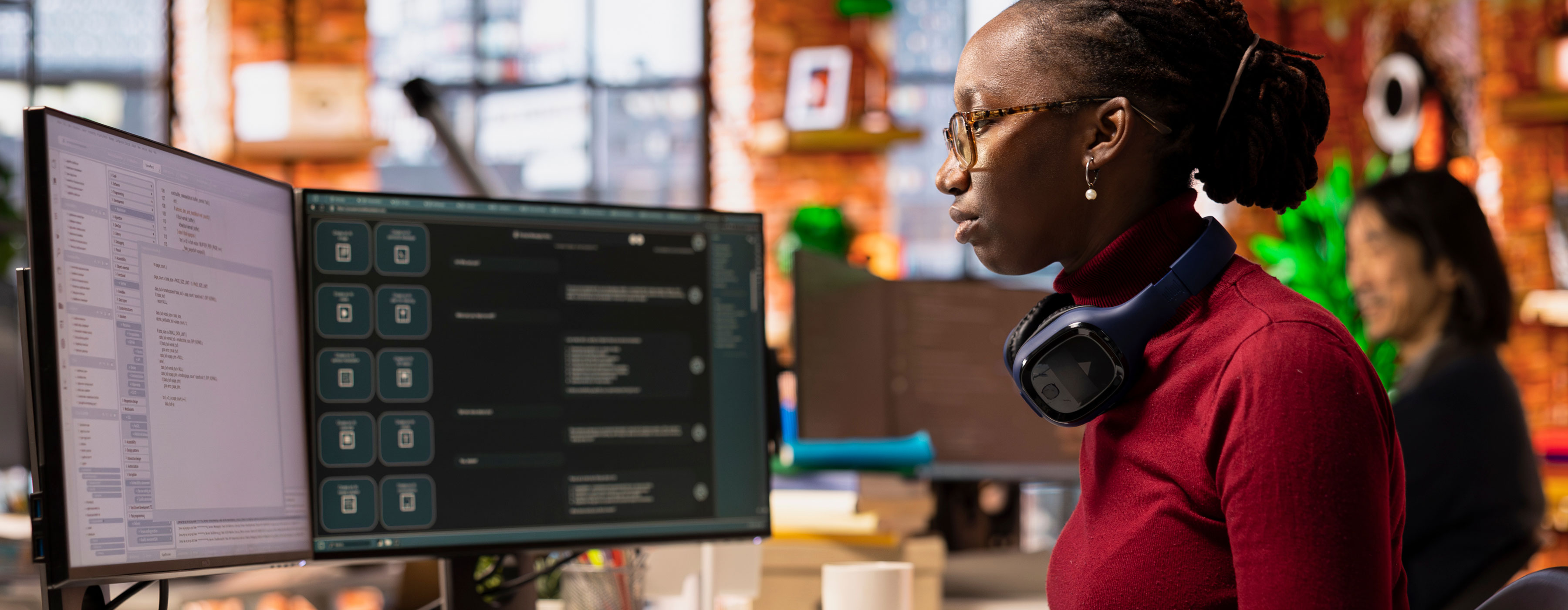 Linguagem de Programação R - foto de uma mulher sentada de perfil, olhando para duas telas de computador e digitando.
