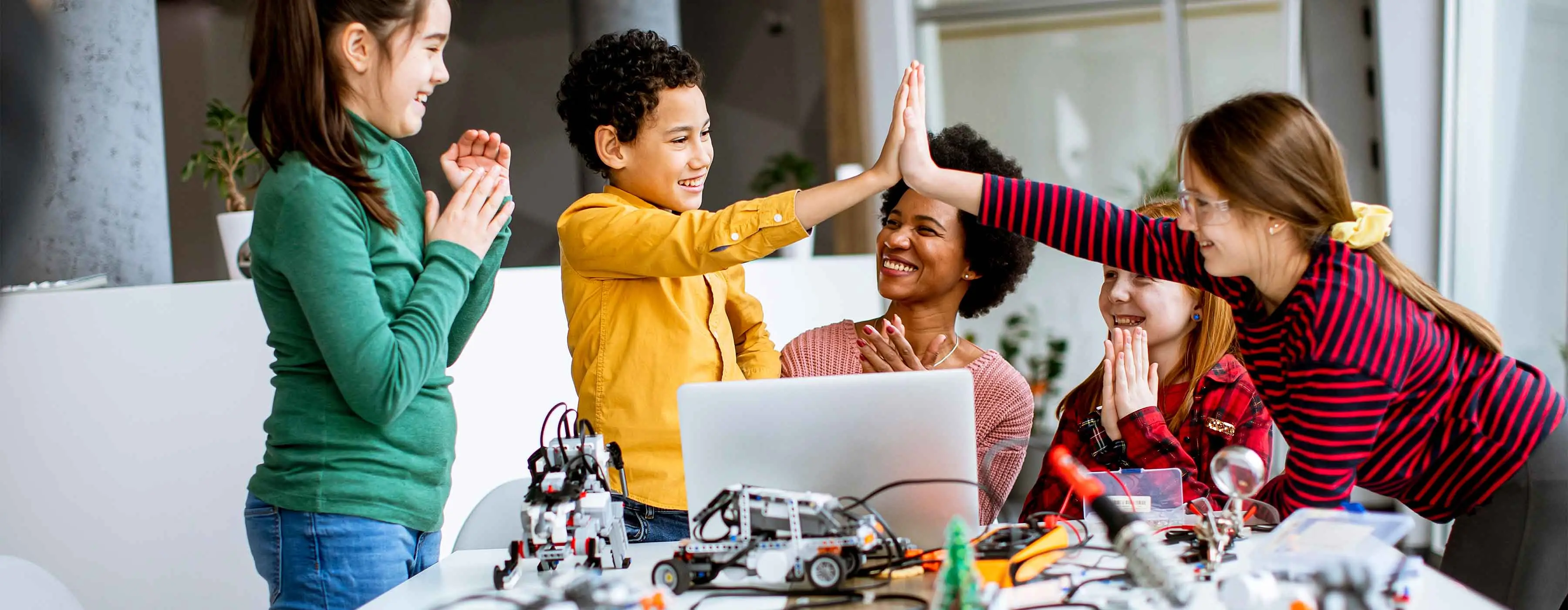 Foto de crianças e uma professora felizes, montando um carrinho eletrônico.