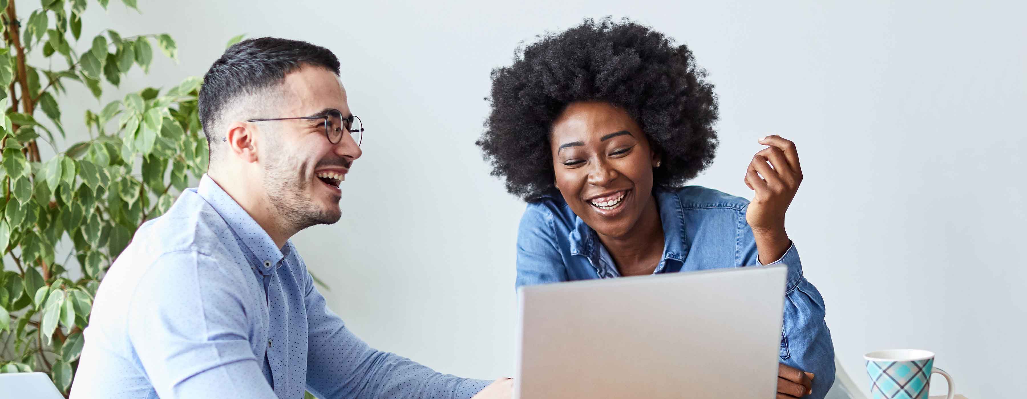 Foto de dois jovens rindo olhando para um computador.