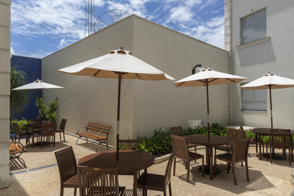 Espaço aberto com ombrelones, jardim, cadeiras, mesas e bancos