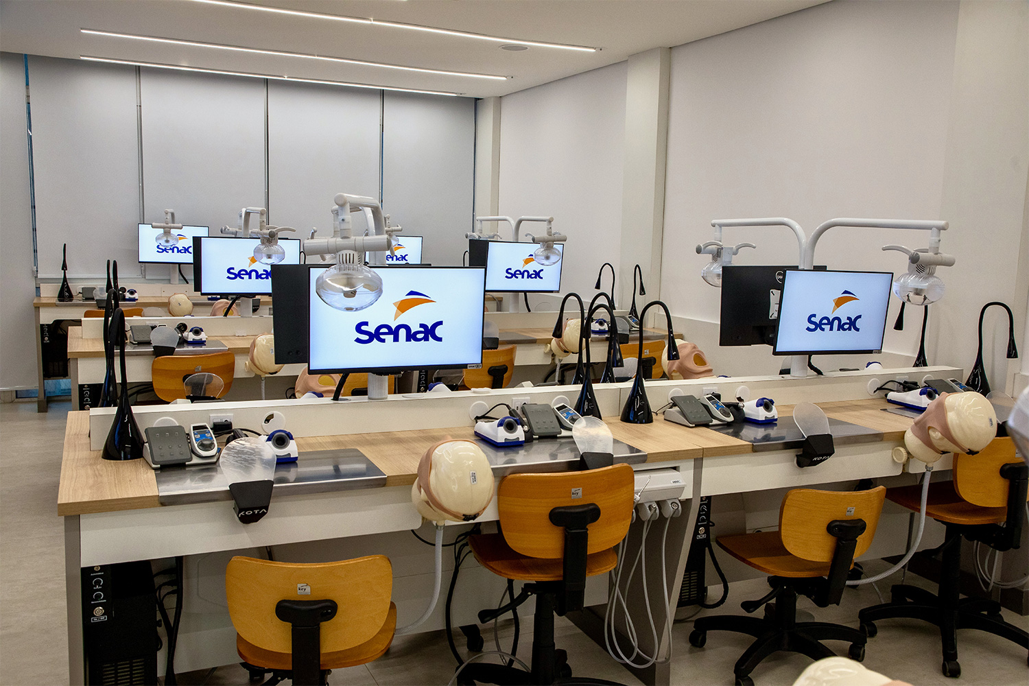 Foto do laboratório com o ponto de vista do fundo da sala, mostrando computadores e equipamentos.
