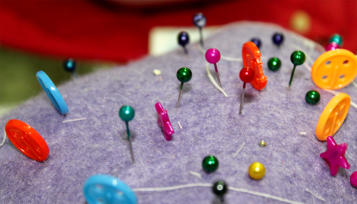 Imagem aproximada de um tecido roxo com agulhas a alfinetes coloridos espetados nele.