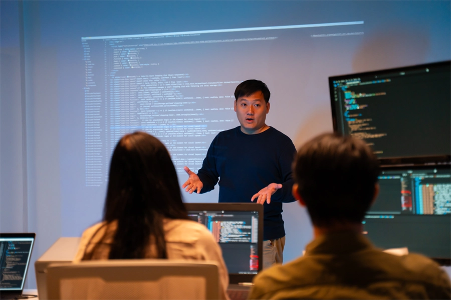 Imagem: professor de curso técnico em desenvolvimento de sistemas dando aula sobre o tema para uma turma em sala de aula.