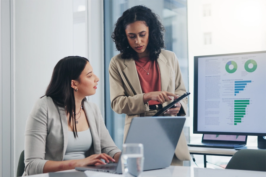 Imagem: duas técnicas em contabilidade conversam em um escritório enquanto analisam gráficos.