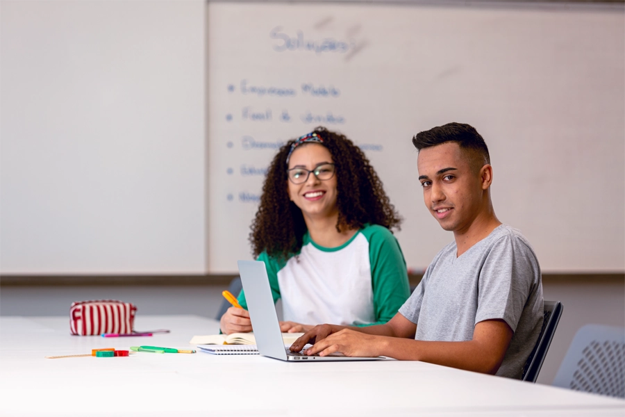 Imagem: dois alunos estudam juntos em sala de aula.