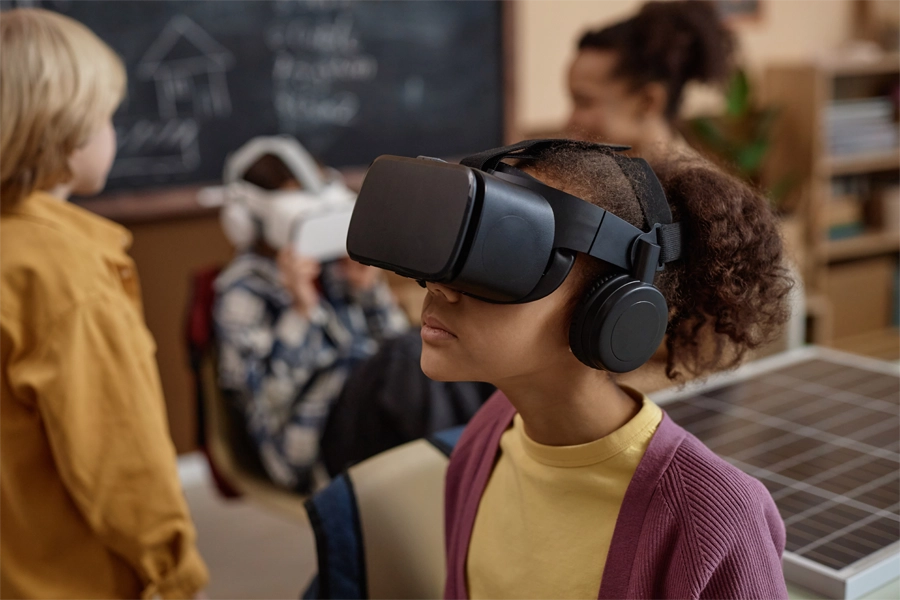 Imagem: em sala de aula, uma aluna utiliza um óculos de realidade virtual para interagir com colegas.