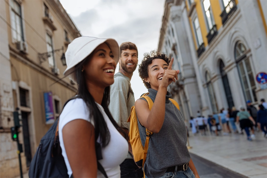 Imagem: três estudantes intercambistas sorriem enquanto olham para a nova cidade e apontam para pontos da cidade.