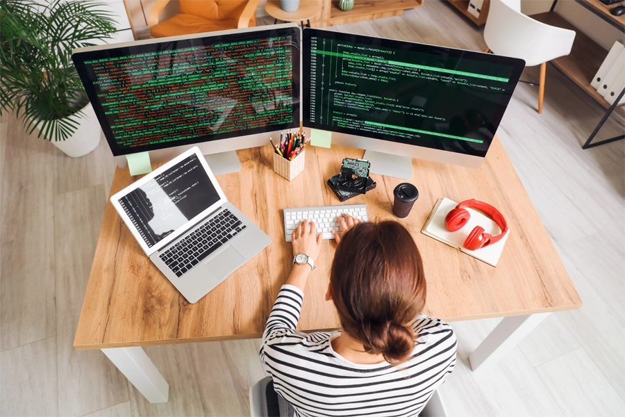 Imagem: técnica em informática para internet trabalha com a ajuda de duas telas em um novo projeto.